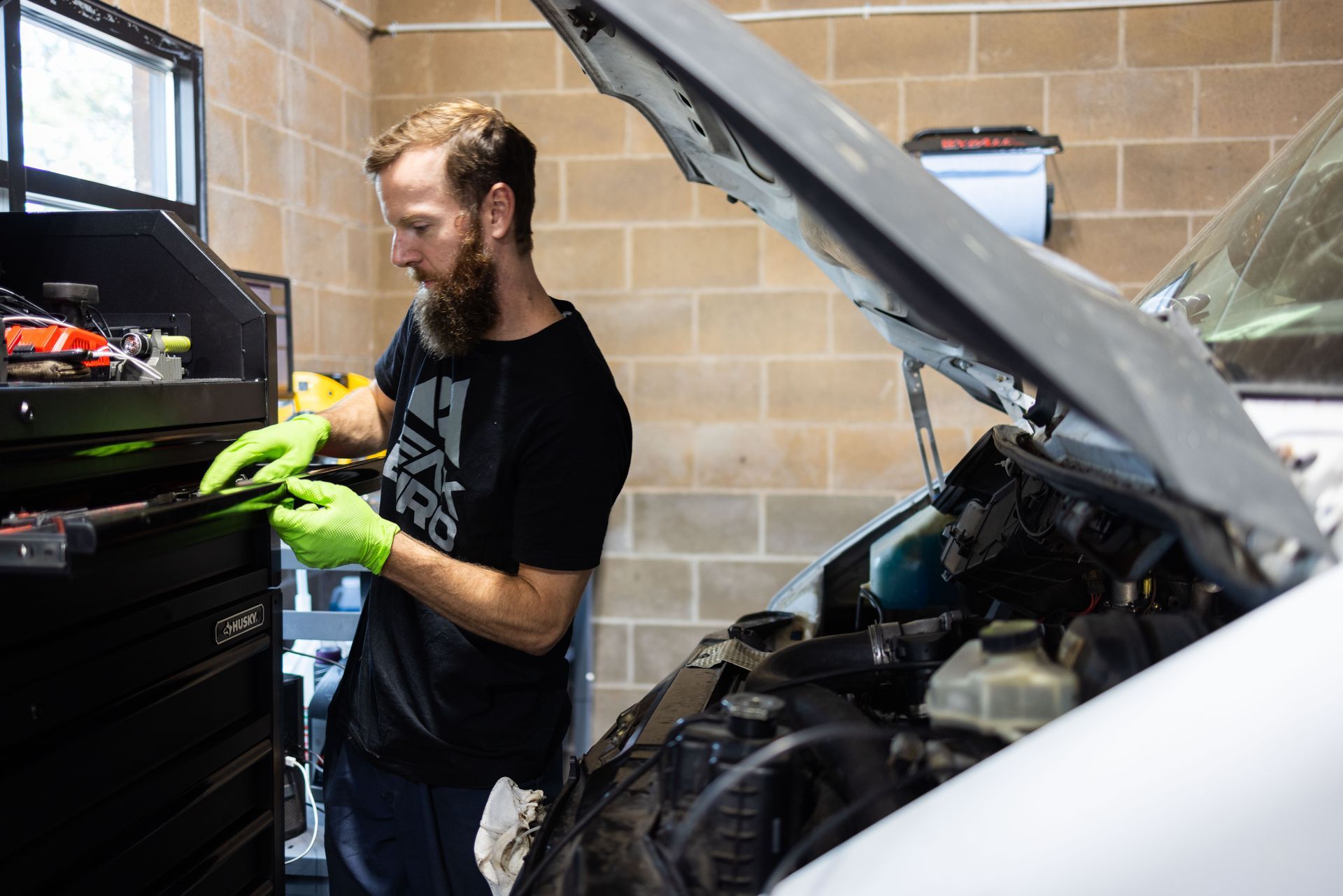 Mechanic with beard and gloves working on a van in a garage, selecting a tool. | Peak Euro