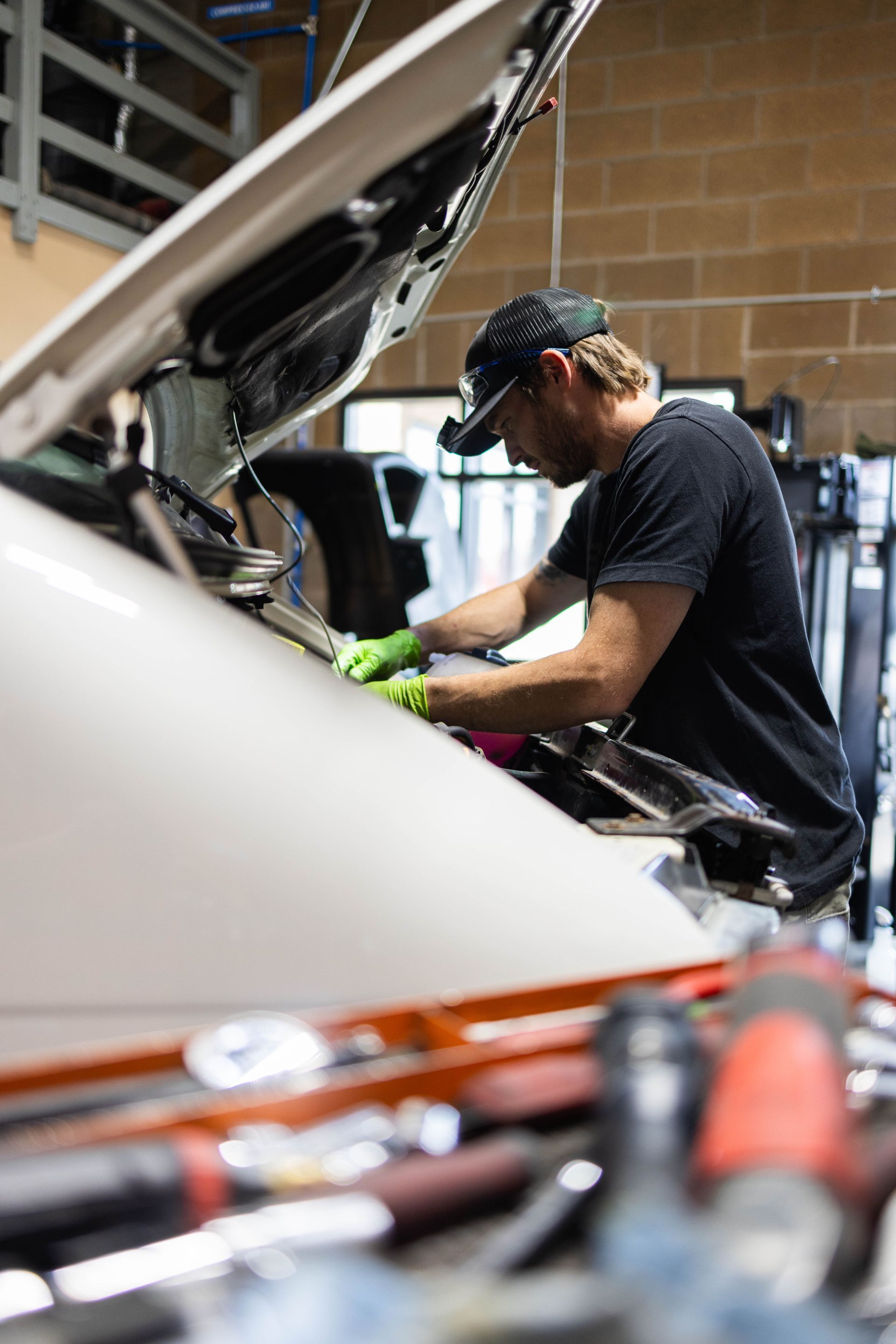 Mechanic works on a car engine in a garage, wearing gloves. | Peak Euro