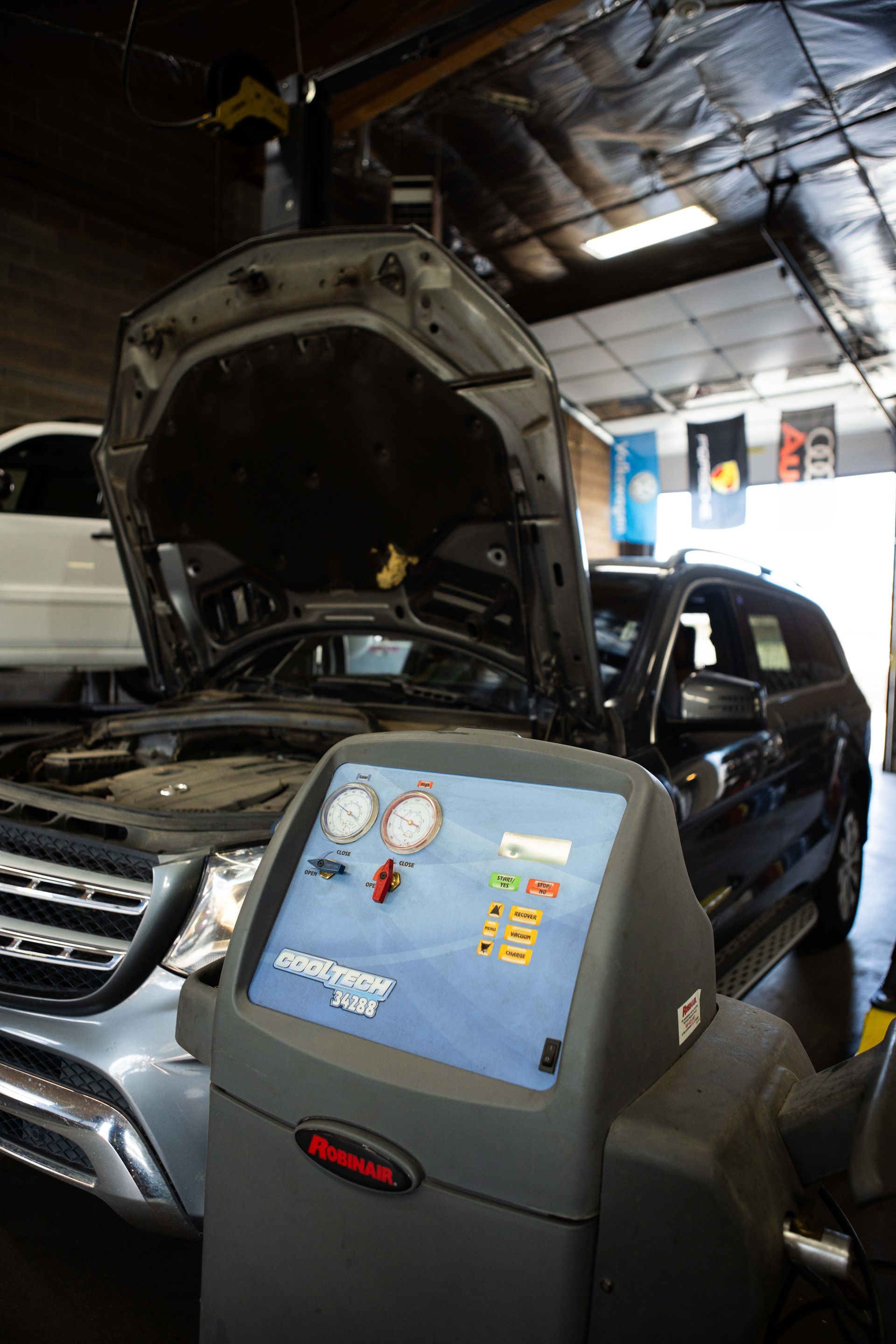 Car in auto repair shop being serviced, with AC recharge machine in front.