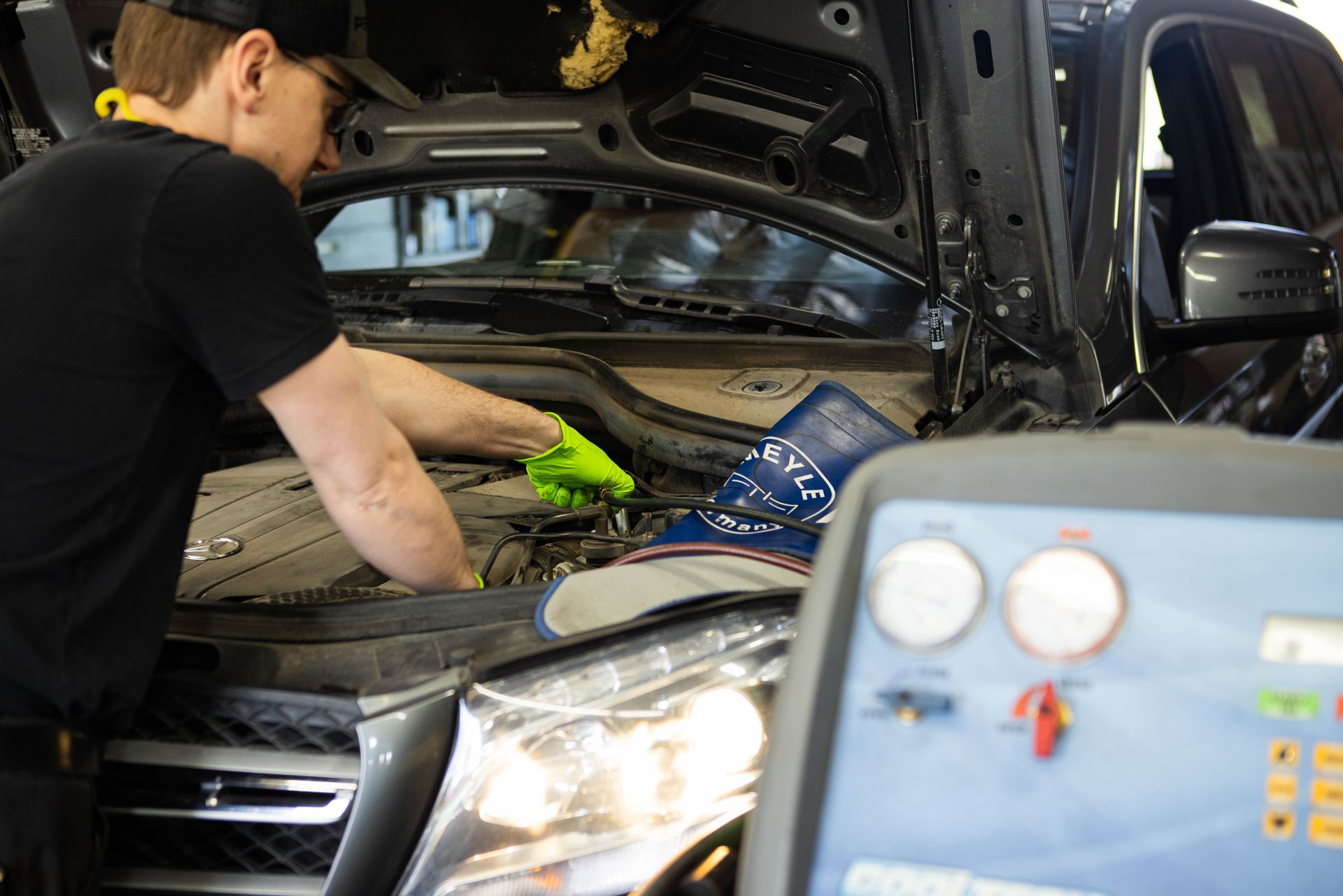 Mechanic servicing a car engine, wearing gloves.  AC machine is visible.
