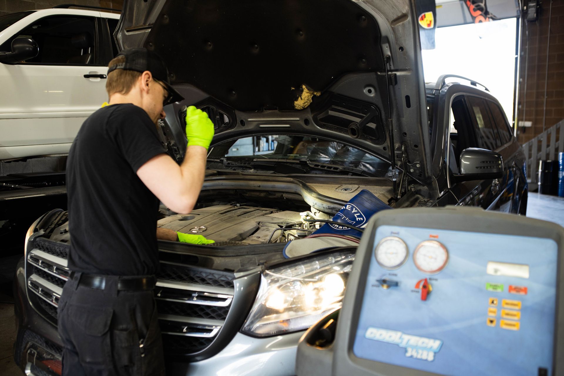 Mechanic inspecting a car engine with a flashlight, surrounded by equipment in a garage. | Peak Euro