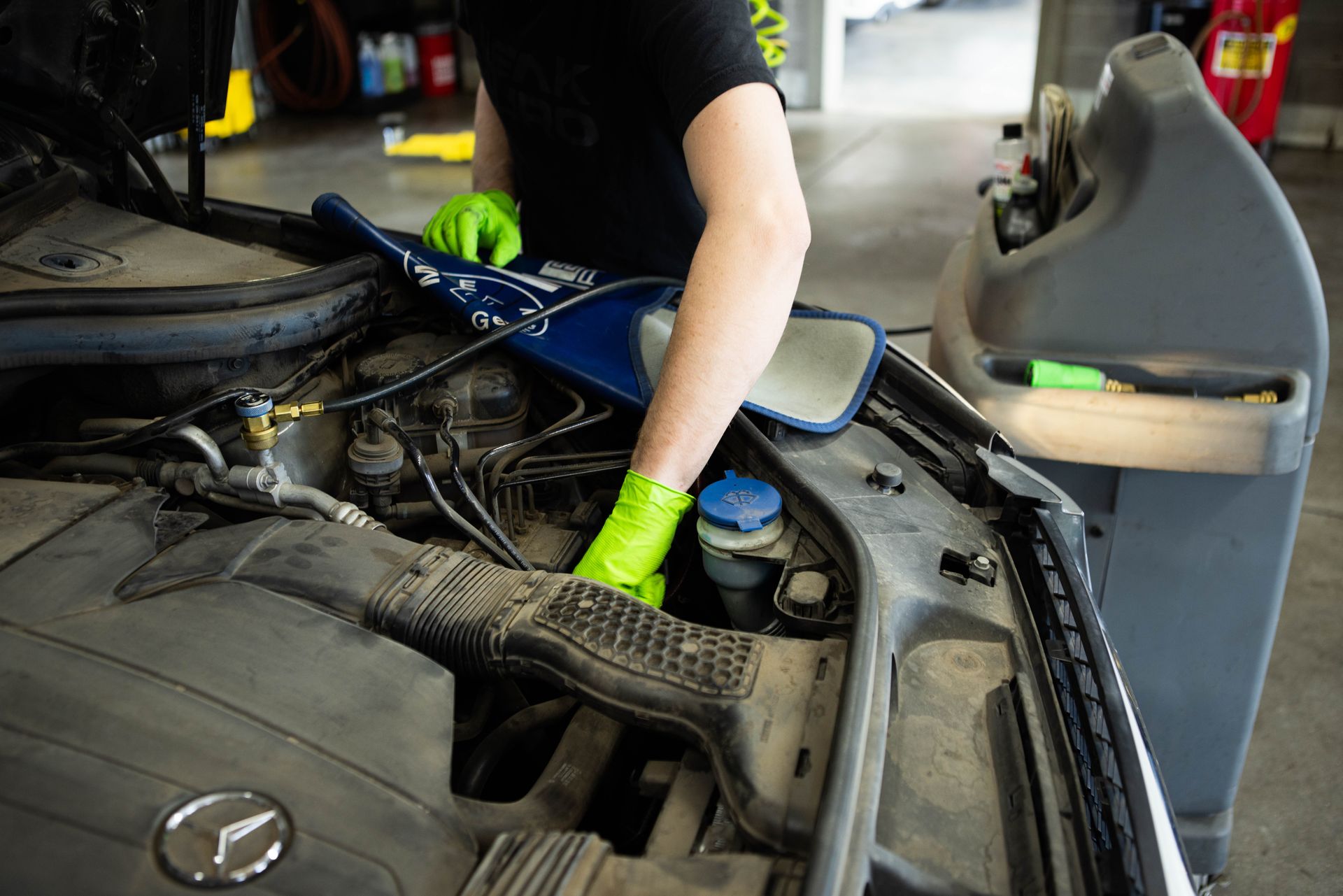 Mechanic in green gloves working on a car engine in a garage. | Peak Euro