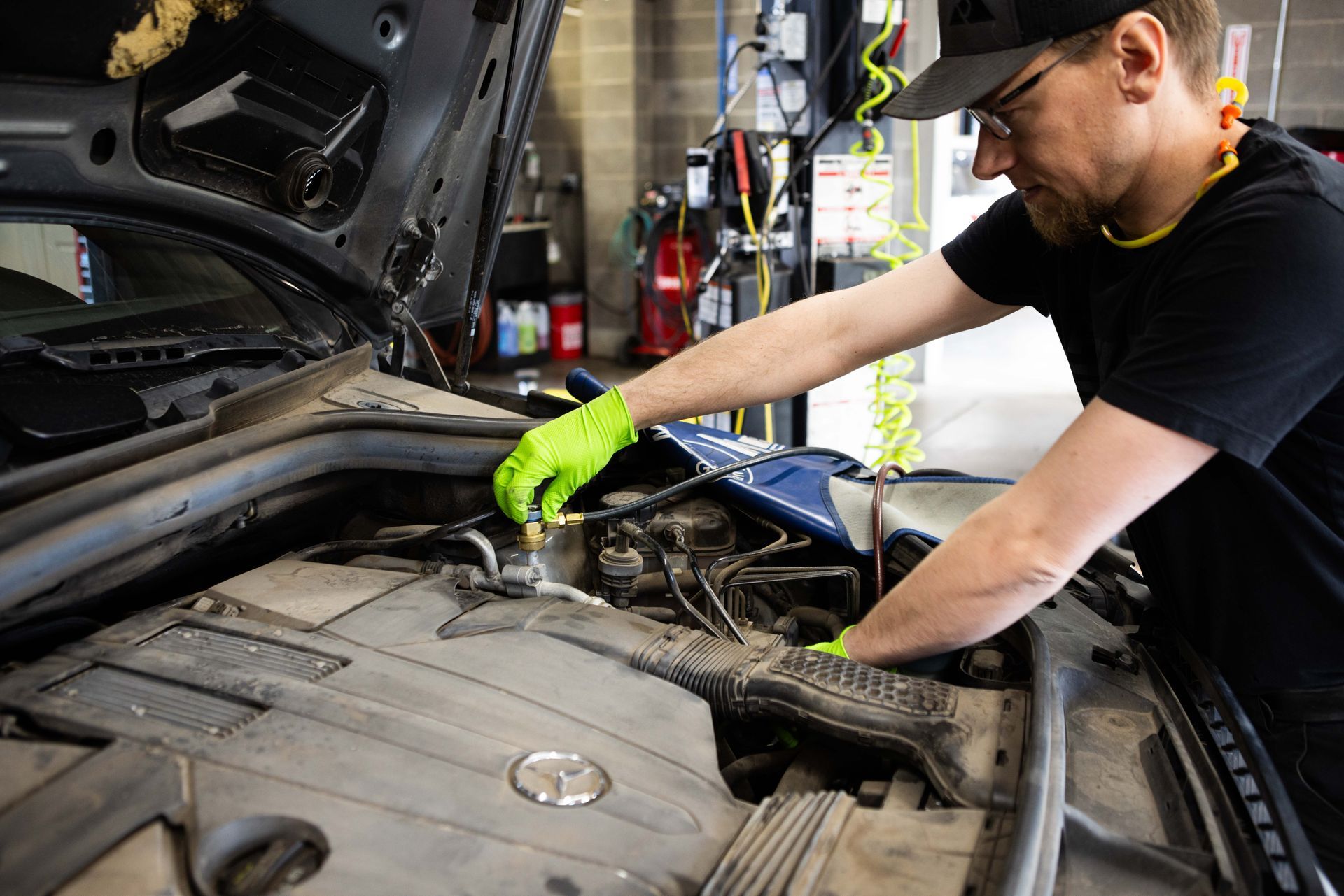 Mechanic in a black t-shirt wearing gloves, working on a car engine in a garage. | Peak Euro