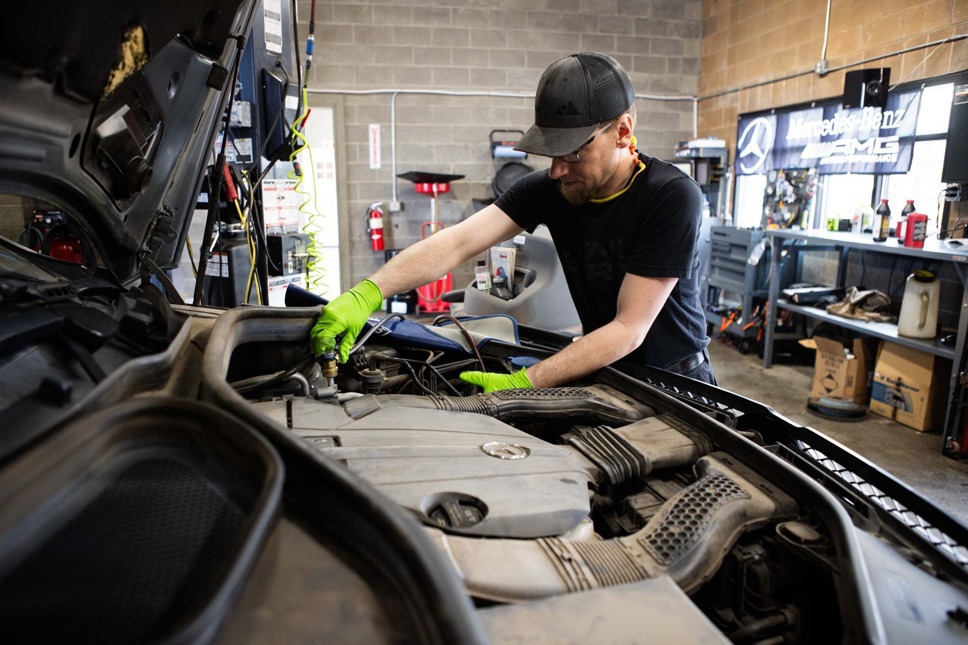 Mechanic working on a car engine in a garage, wearing gloves and cap. | Peak Euro