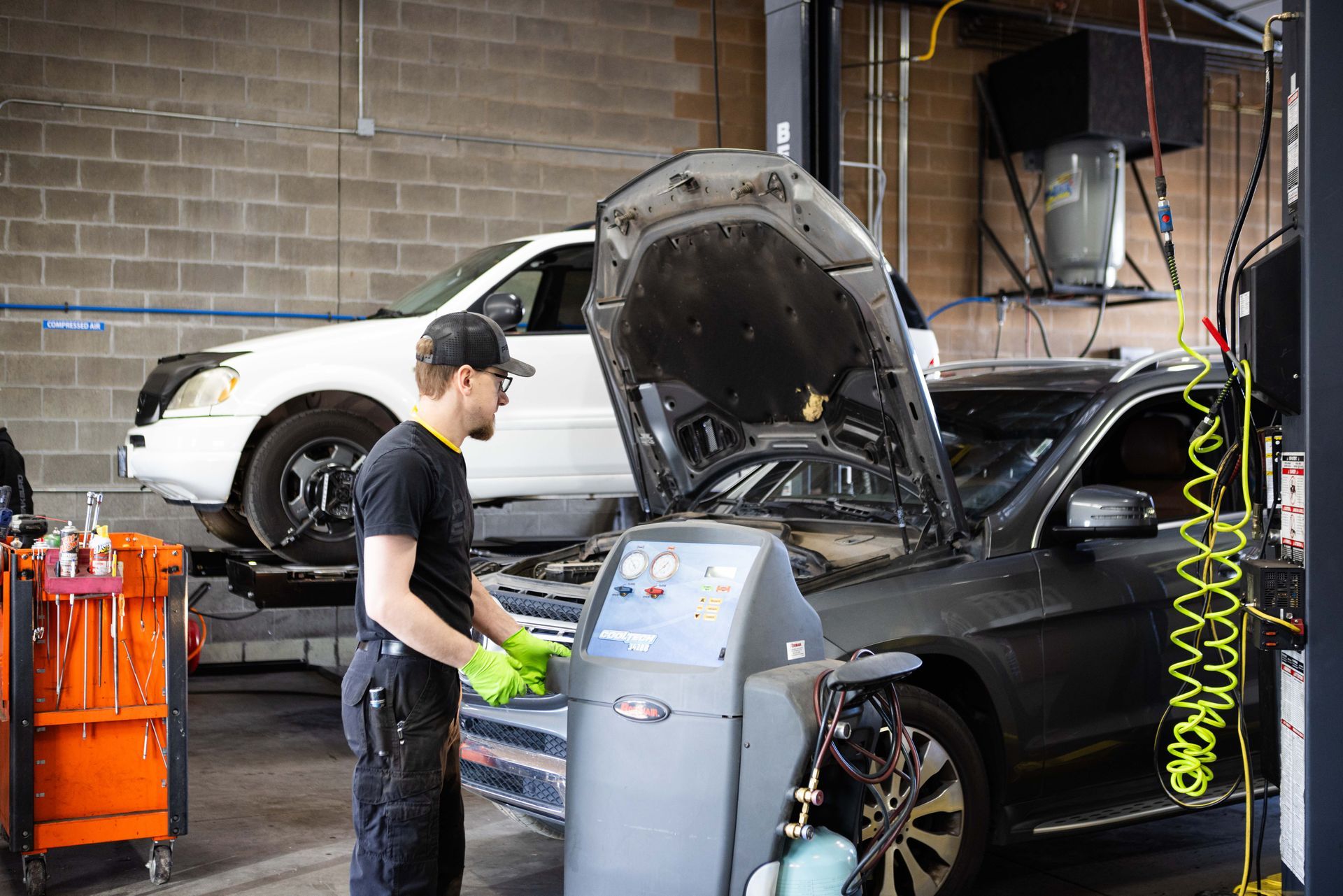 Mechanic working on car in a garage, using machine. Another car on lift in background. | Peak Euro