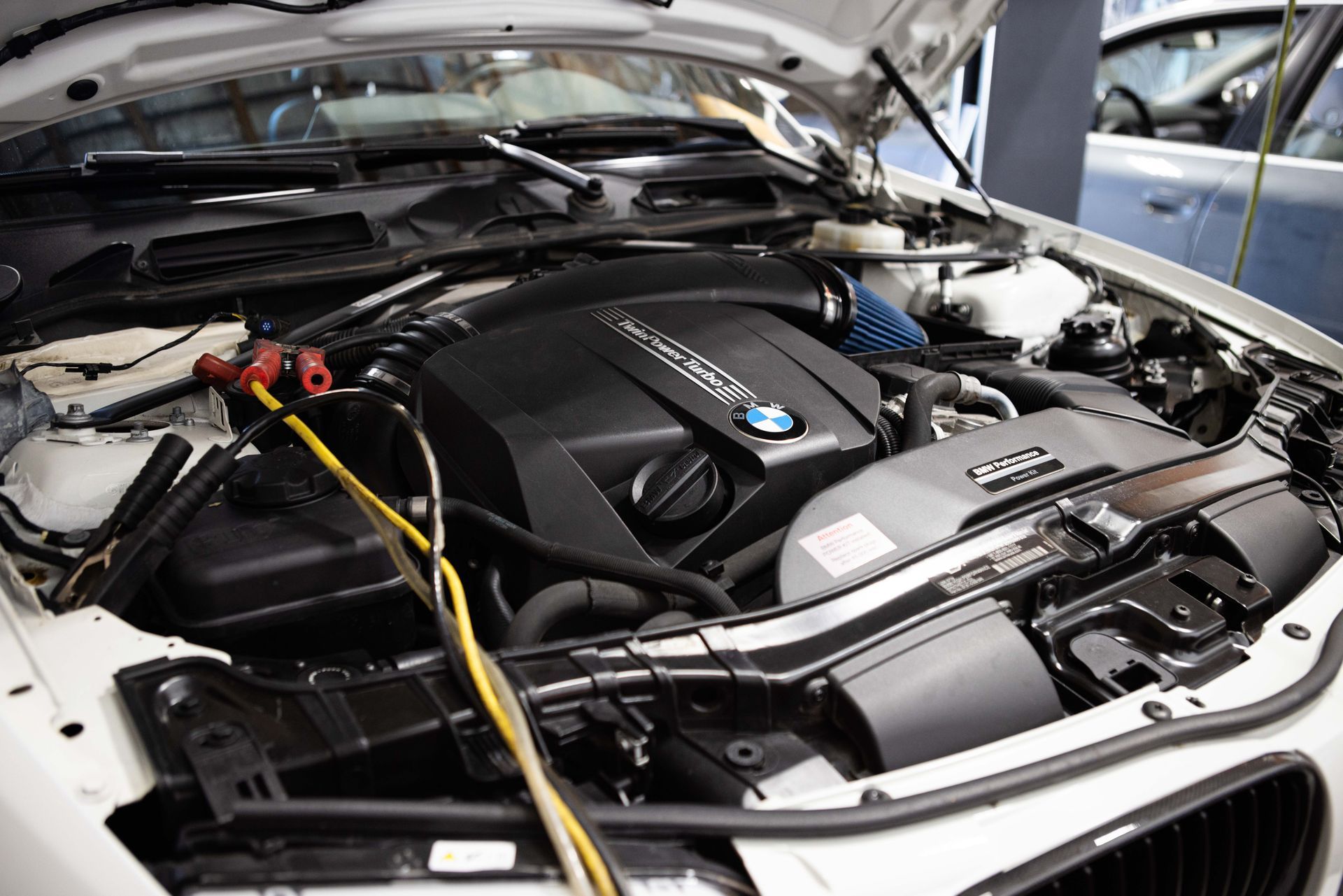 White BMW car engine bay, open hood. Electrical cables attached, likely for repair. | Peak Euro