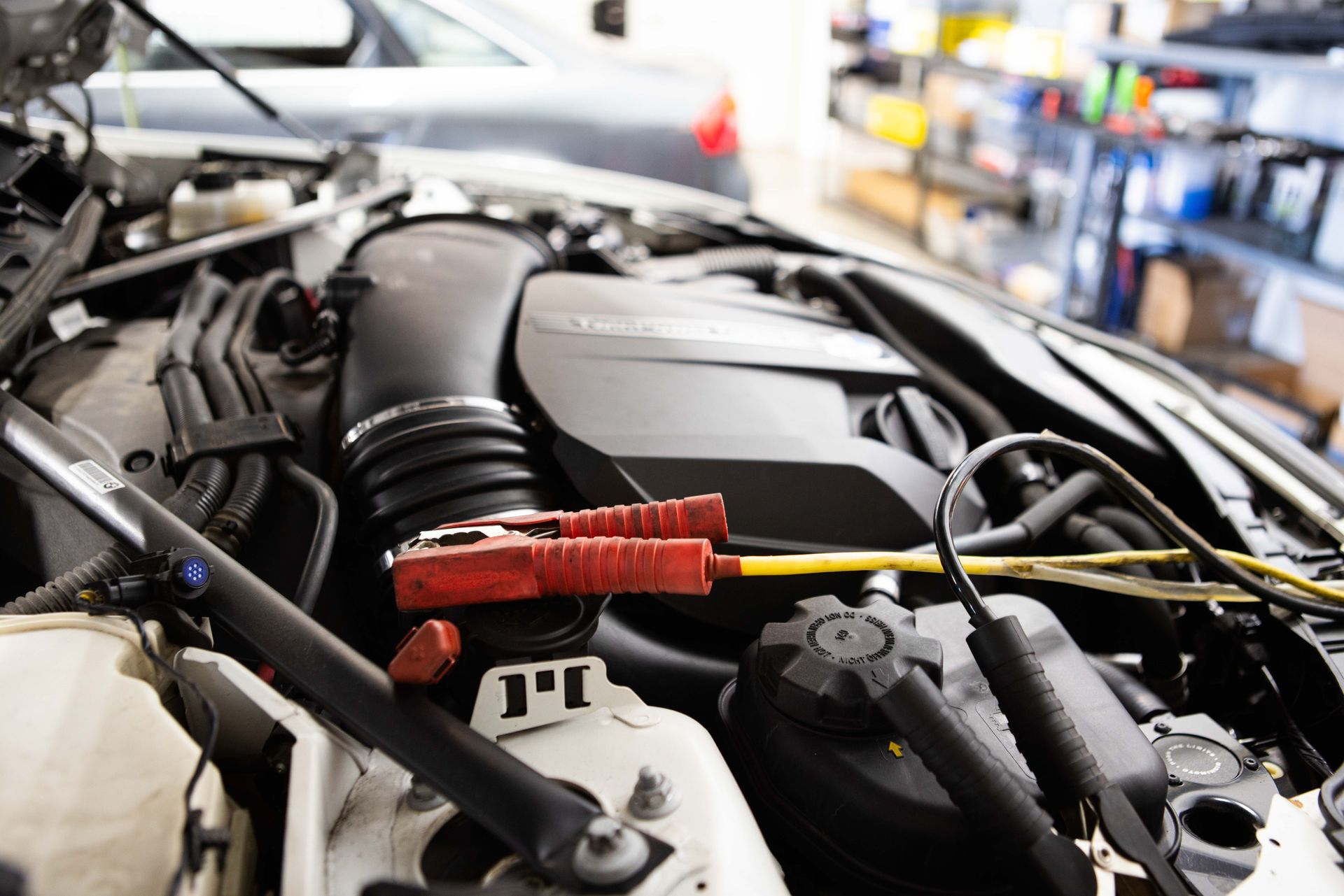 Car engine with red and black jumper cables connected; in a shop.