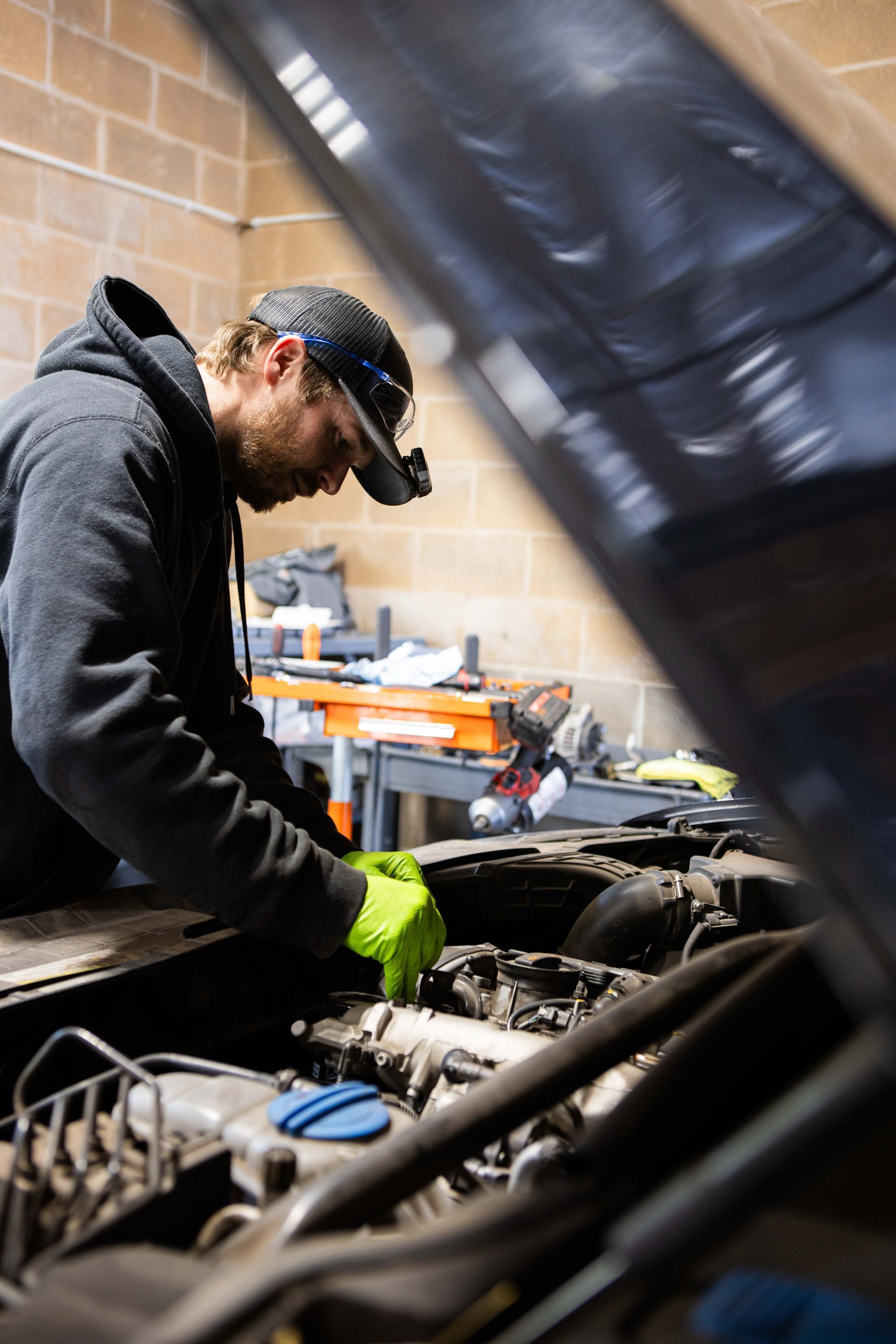 Mechanic working on a car engine with a headlamp, wearing gloves, in a garage. | Peak Euro