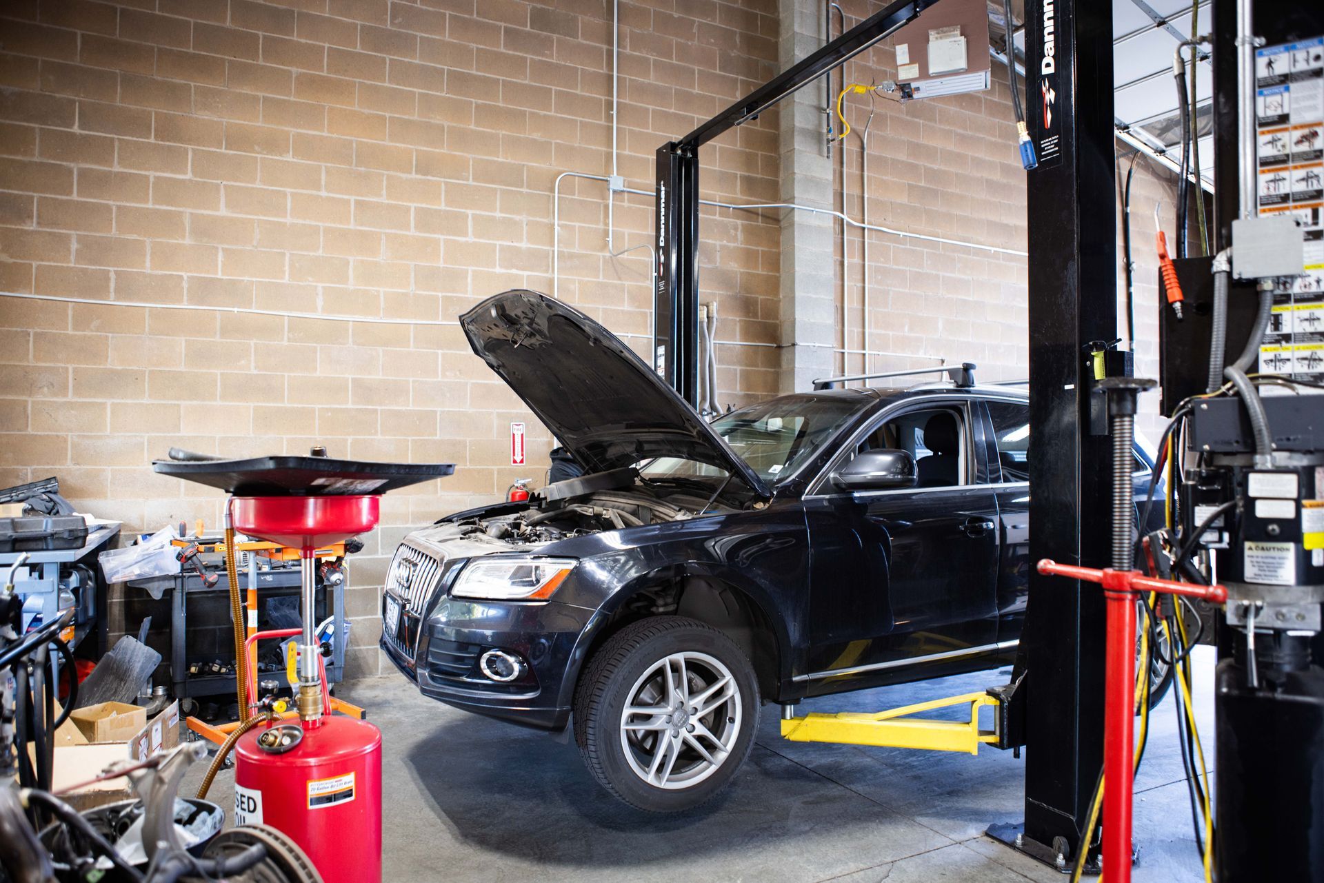Black SUV being repaired in an auto shop, hood open, raised on a lift. | Peak Euro