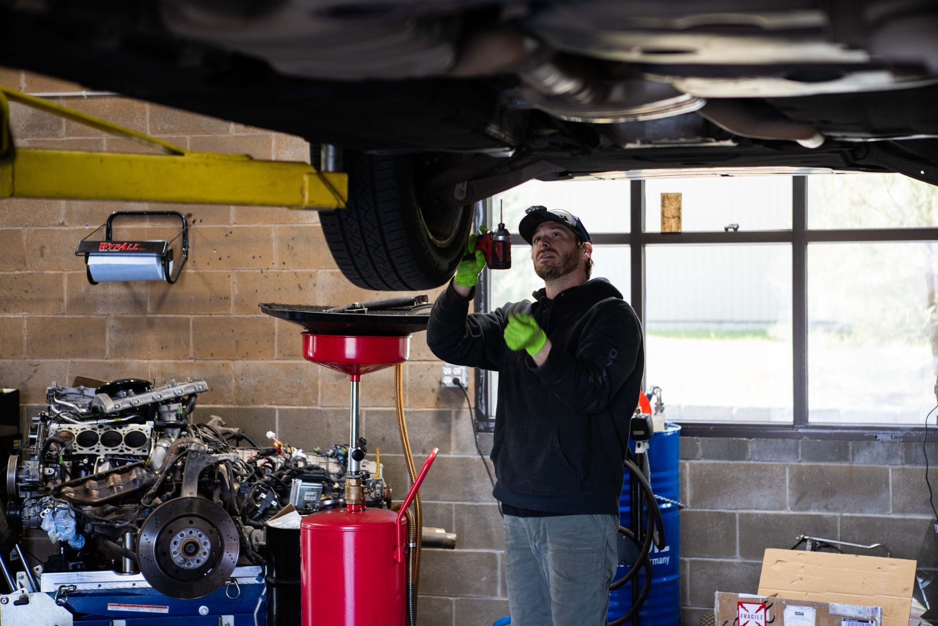 Mechanic working on a car raised on a lift in a garage. He wears a hat and gloves. | Peak Euro