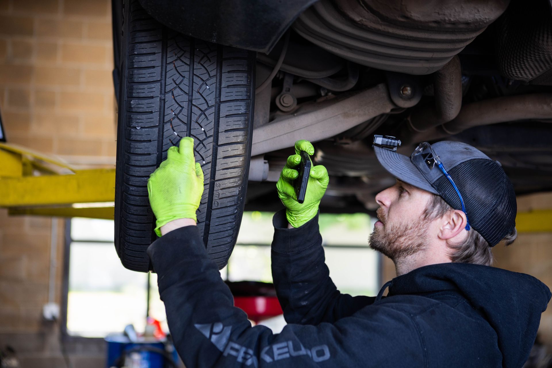 Mechanic inspecting a car tire on a lift. Wearing gloves, holding a tool. | Peak Euro