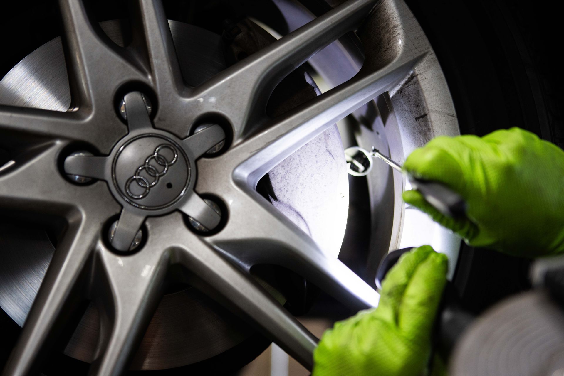 Hands in green gloves inspect an Audi wheel, using a tool to check the tire.