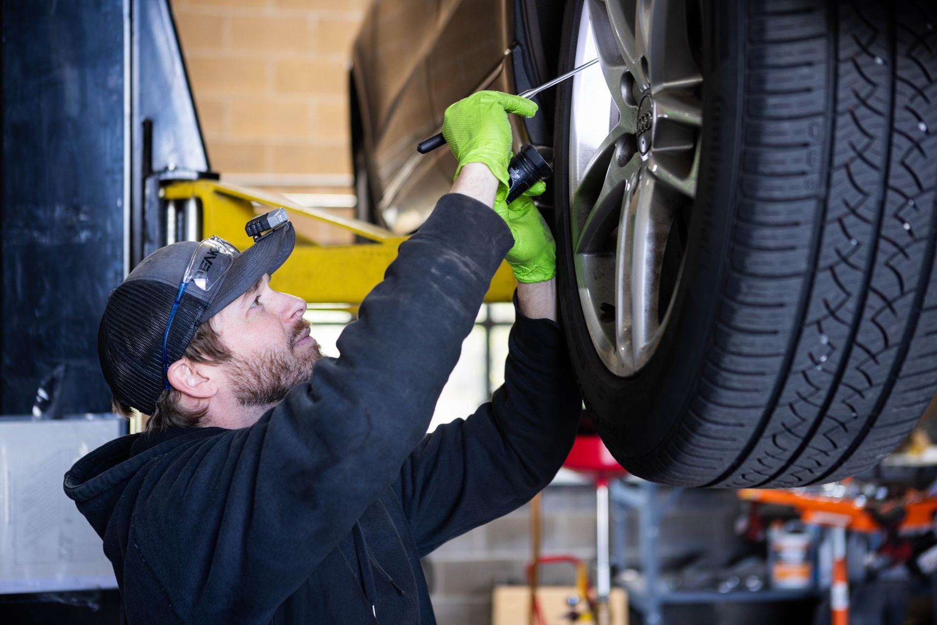 Mechanic working on a car tire with green gloves, in a garage.