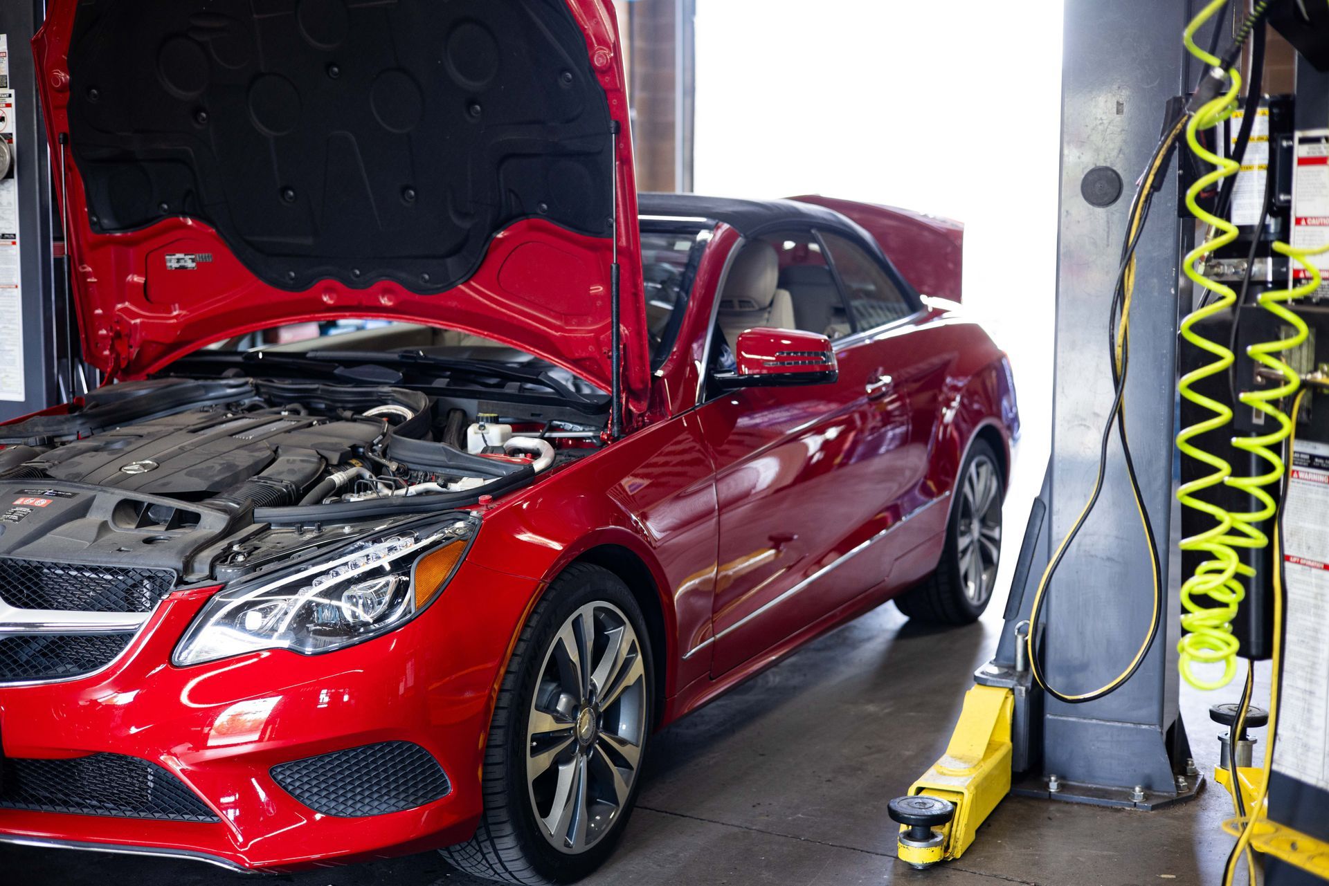 Red car with open hood in a repair shop.