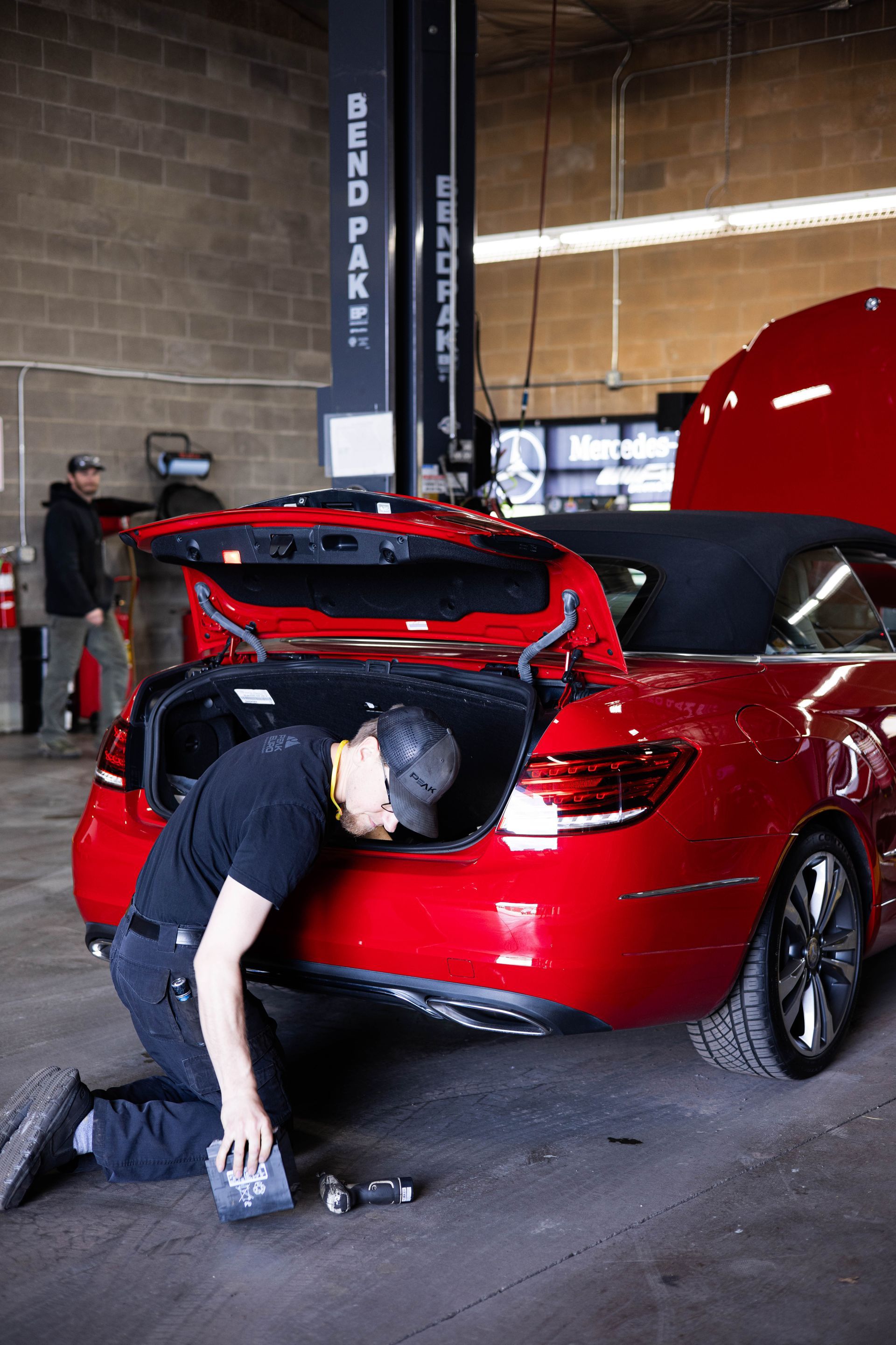 Mechanic working on red convertible's trunk in a garage. | Peak Euro