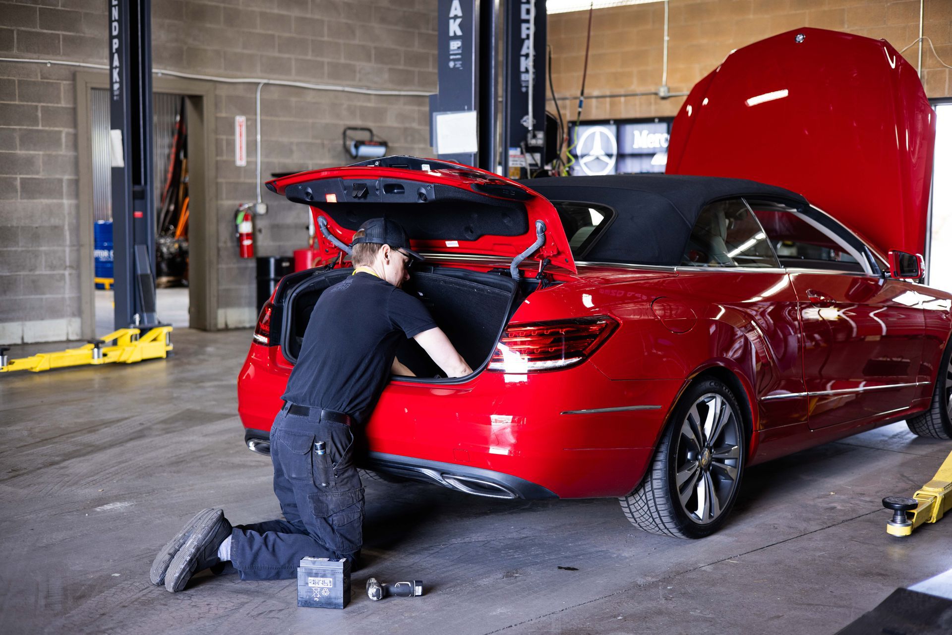 Mechanic working on a red convertible in a garage with the trunk and hood open. | Peak Euro
