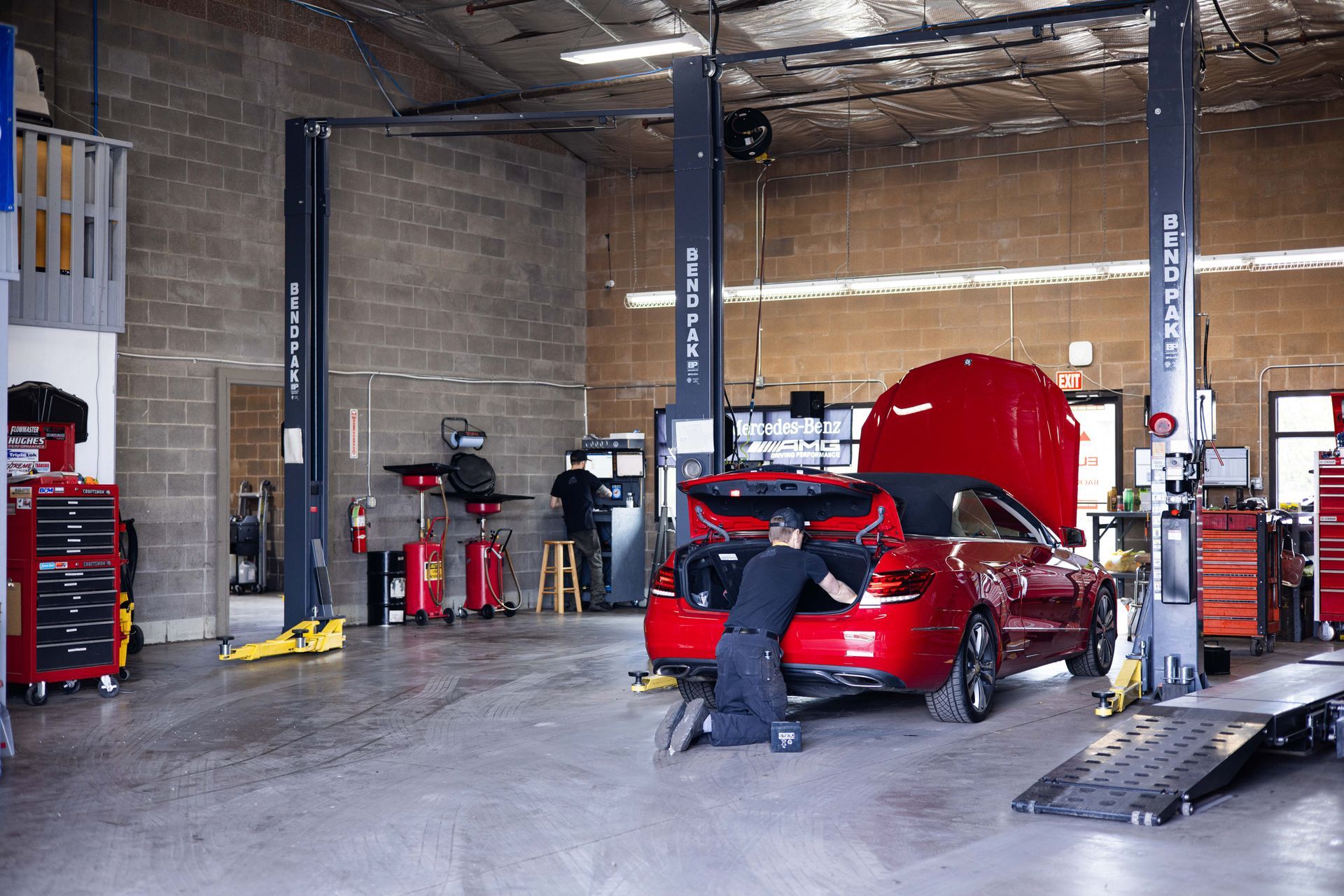 Mechanic working on a red car in an auto repair shop, using tools. | Peak Euro