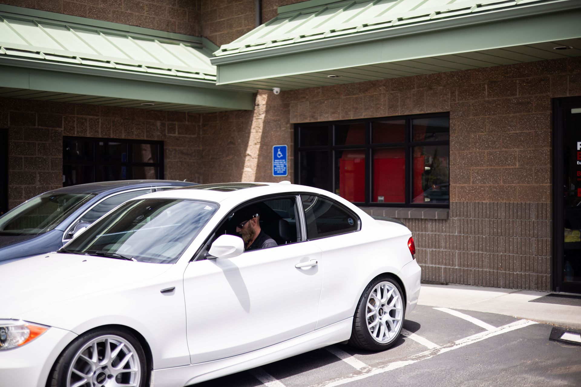 White BMW coupe parked outside a building with accessible parking.