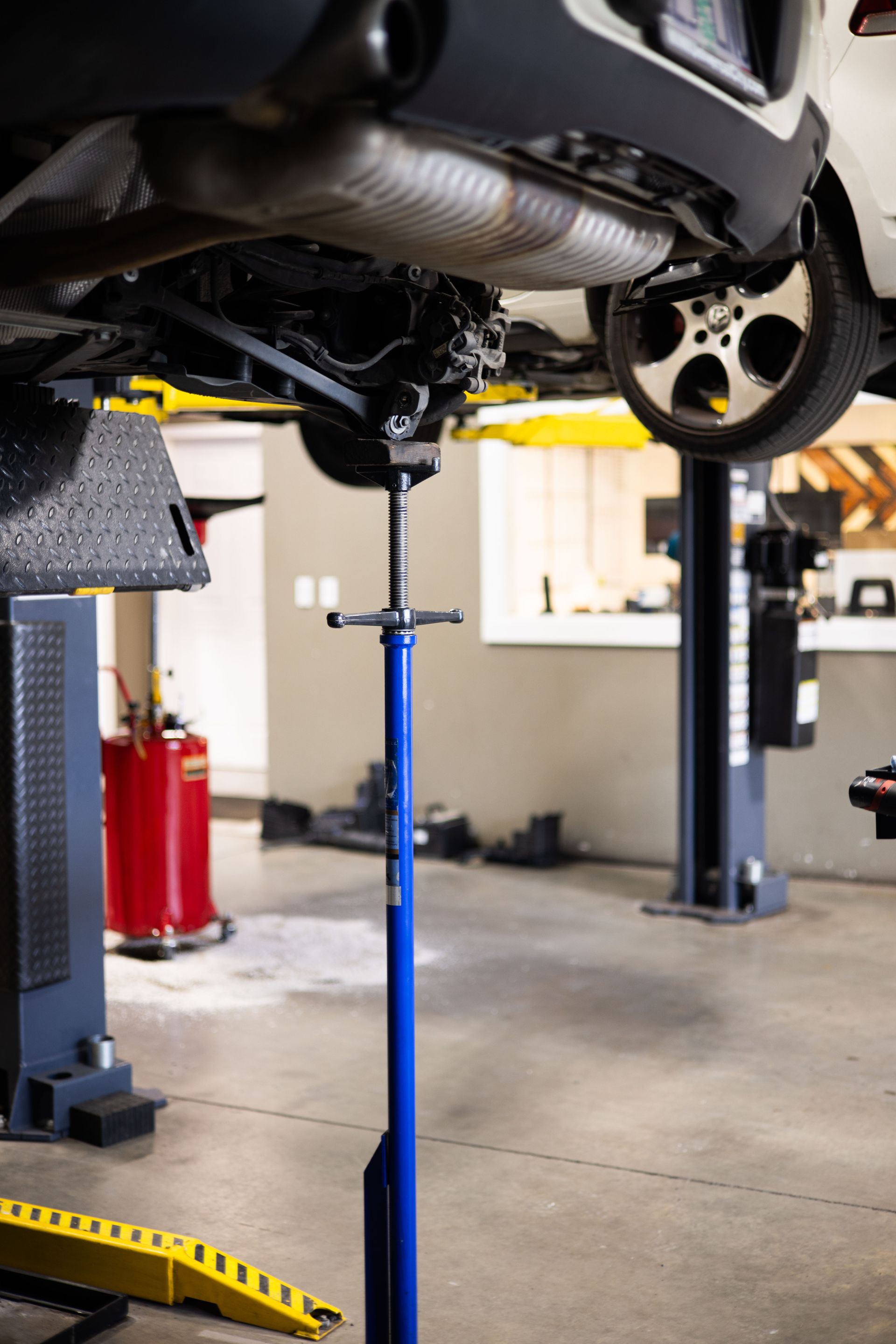 Blue jack supporting a car's undercarriage in a garage. The car is on a lift, the wheel is visible.