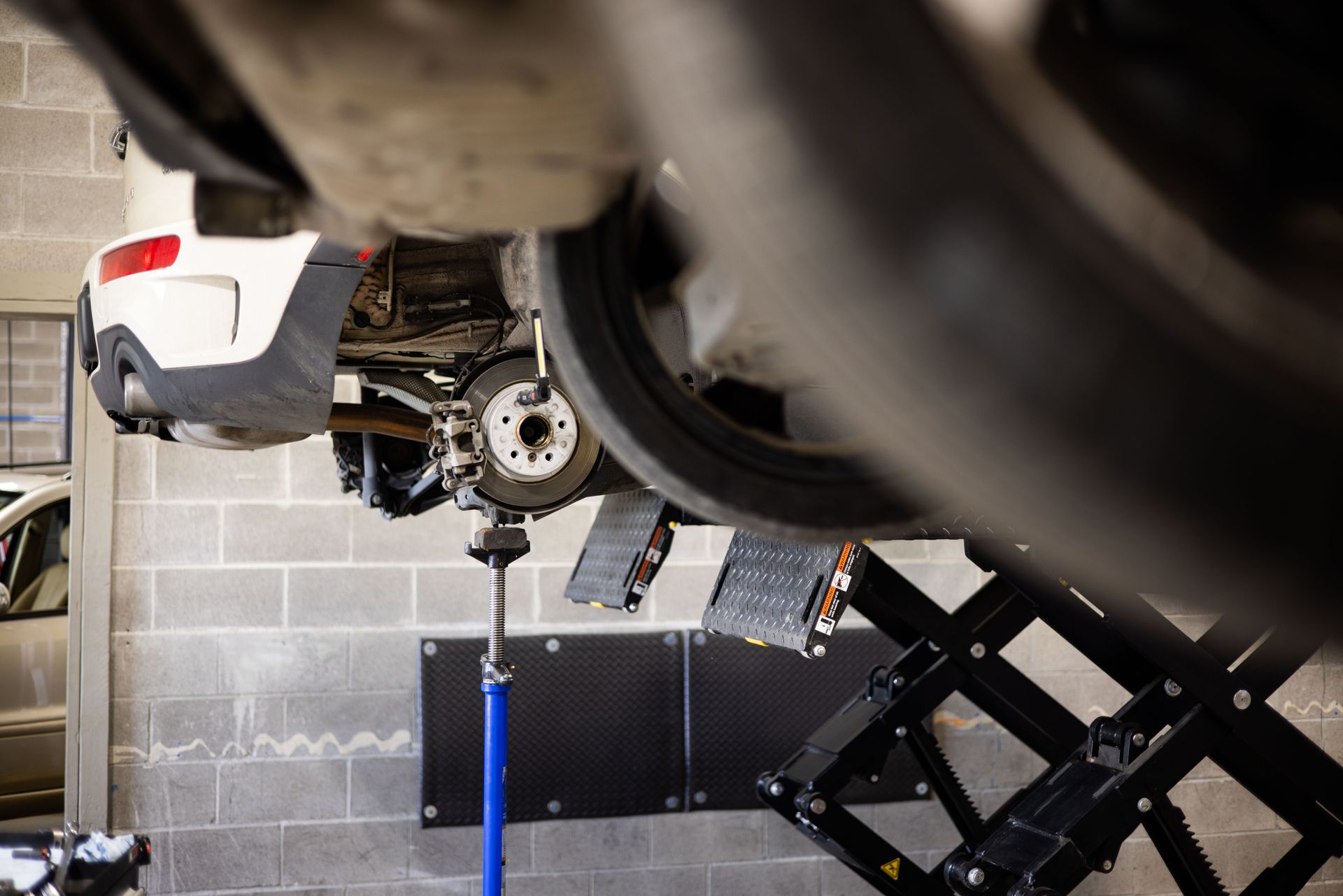 Car on a lift, revealing undercarriage and wheel components in a garage.