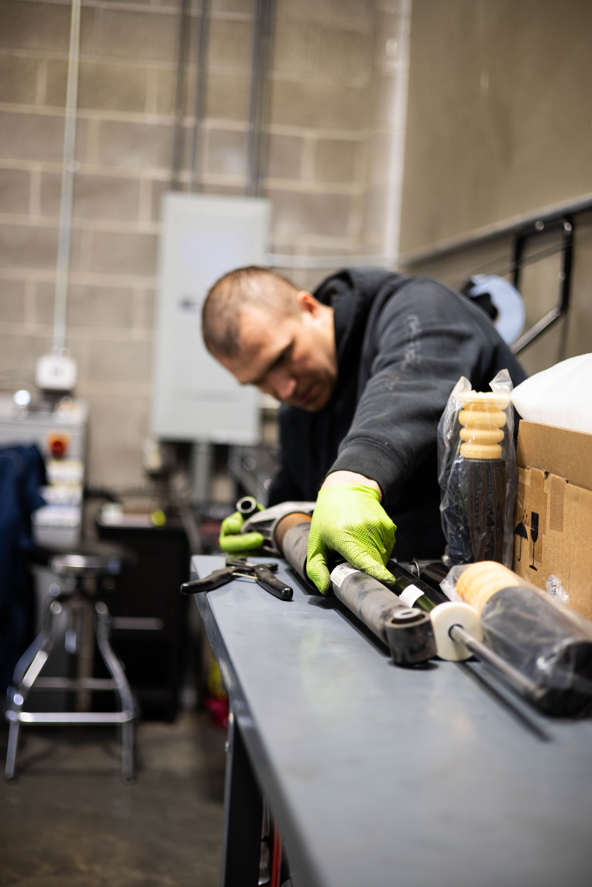 Mechanic in a garage wearing gloves, working on car parts laid on a gray table.