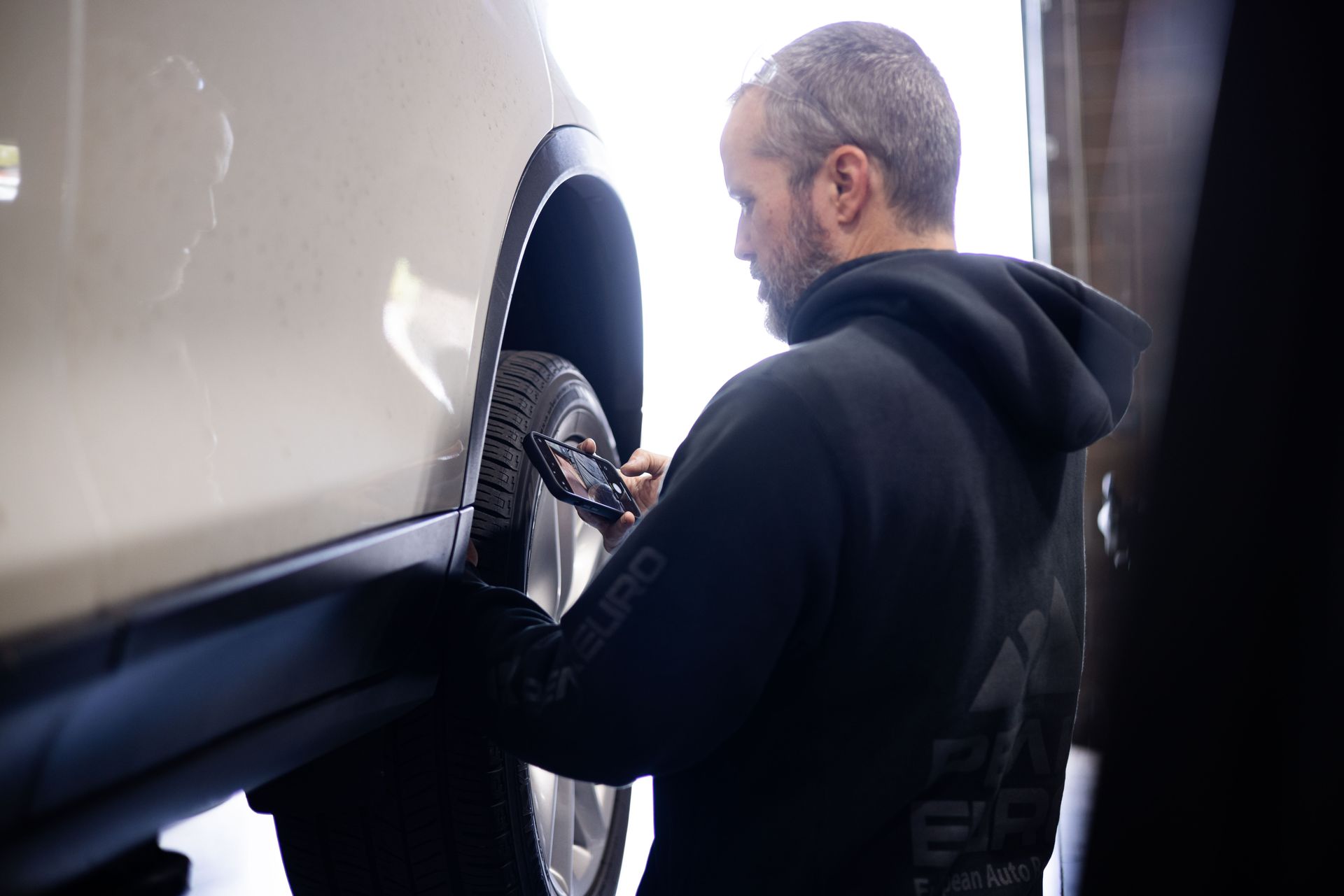 Mechanic inspecting a tire on a lifted, beige car in a garage.