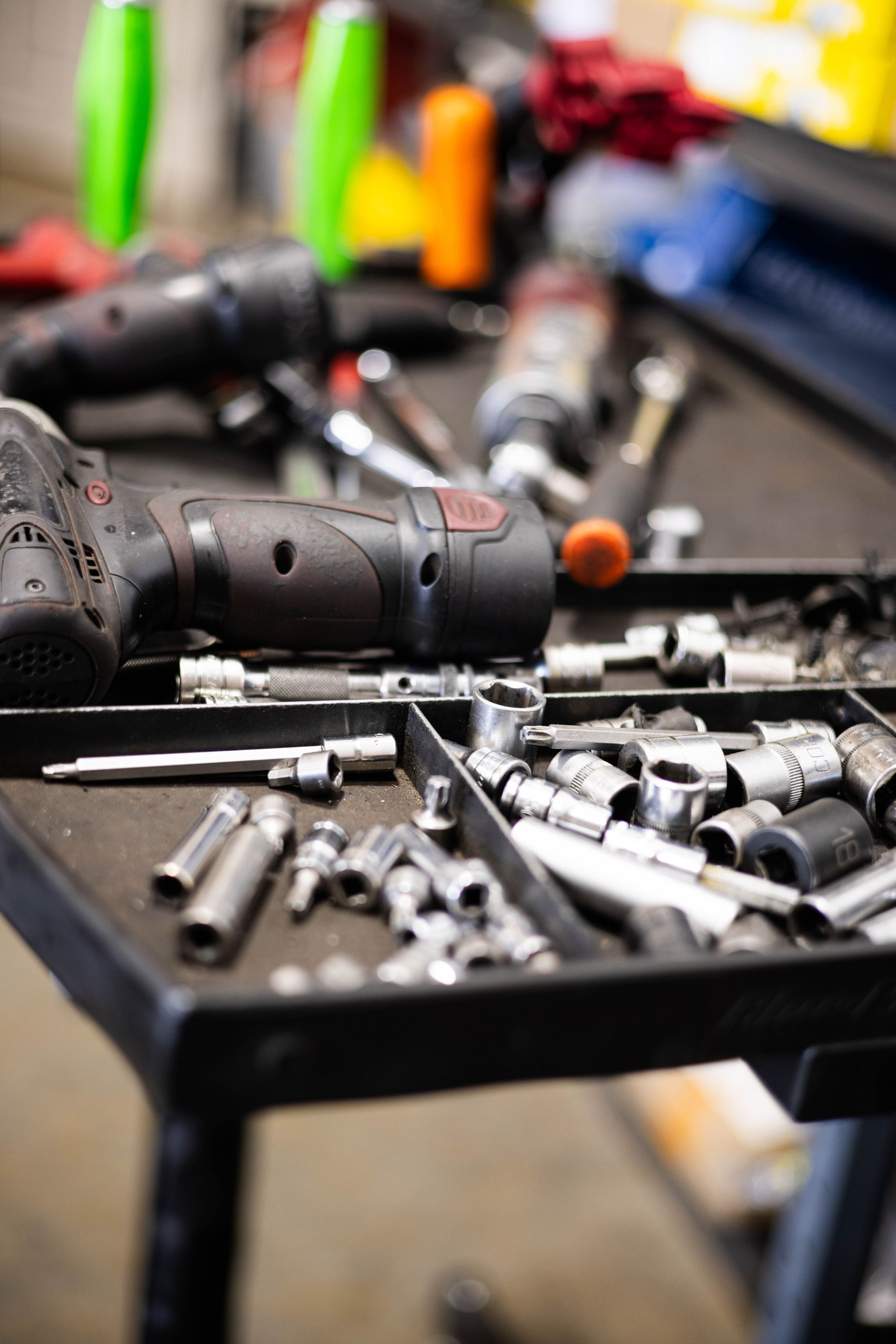 A black tool cart with a tray of tools, including power drills and sockets, in a garage setting.