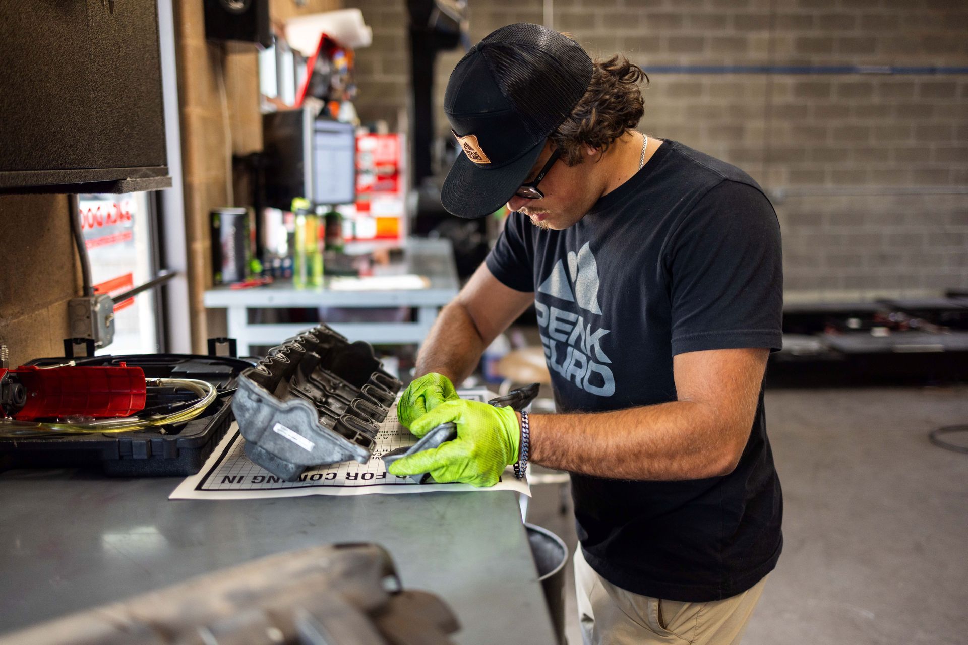 Man in a workshop wearing a hat and gloves inspecting a part on a table. | Peak Euro