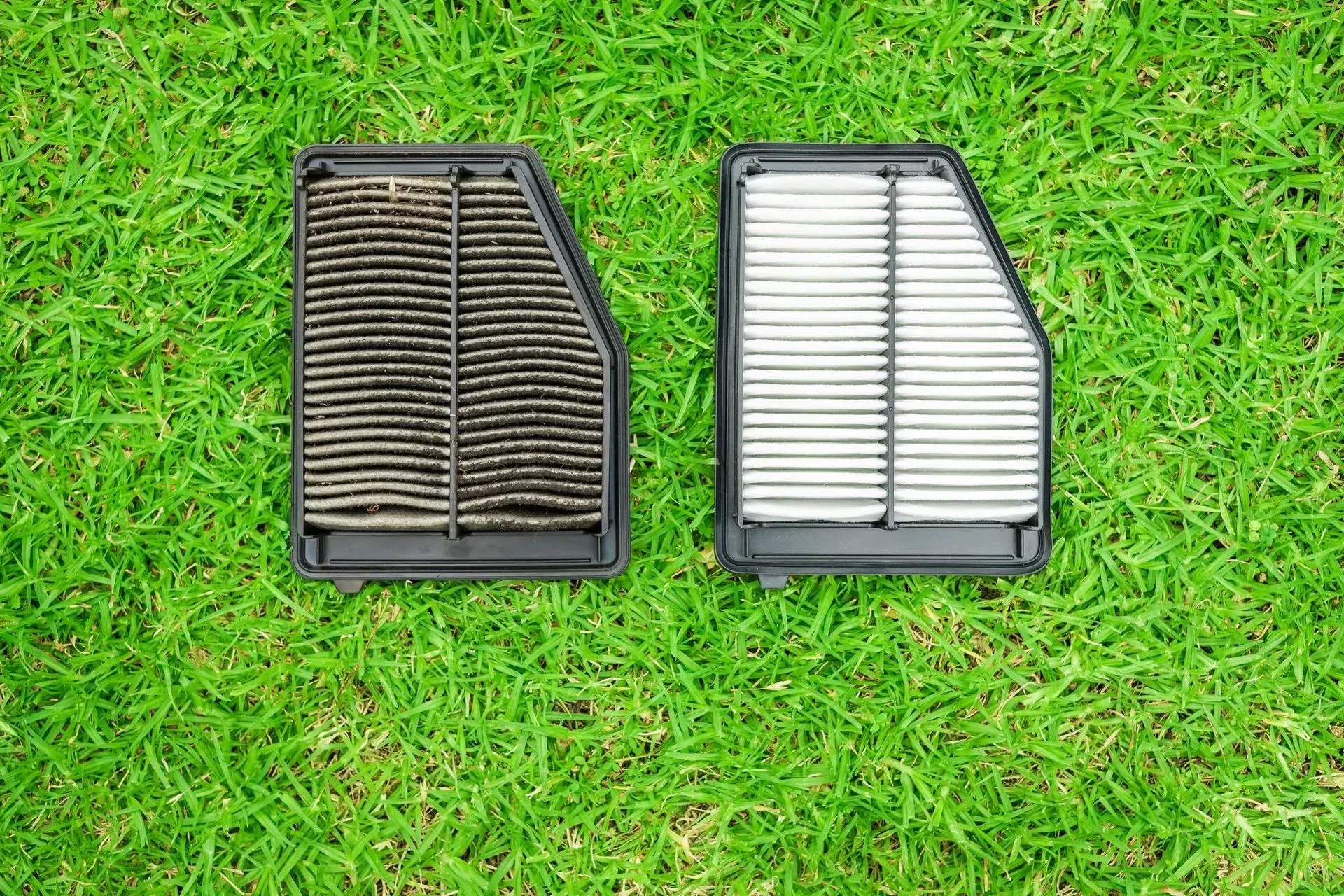 Two rectangular car air filters, one dirty, one clean, on green grass.