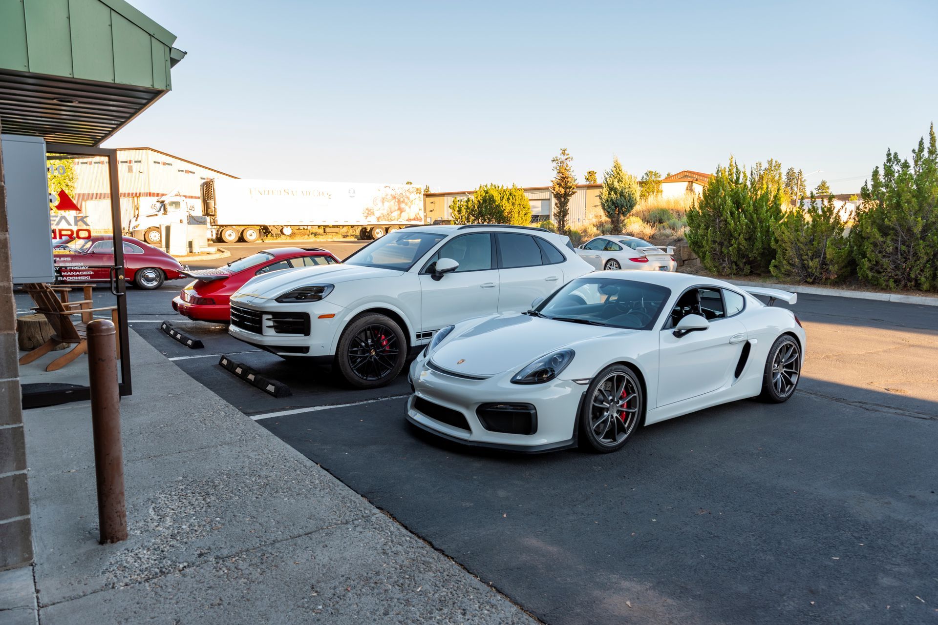 White Porsche Cayman and SUV parked outside. Red car in background. | Peak Euro