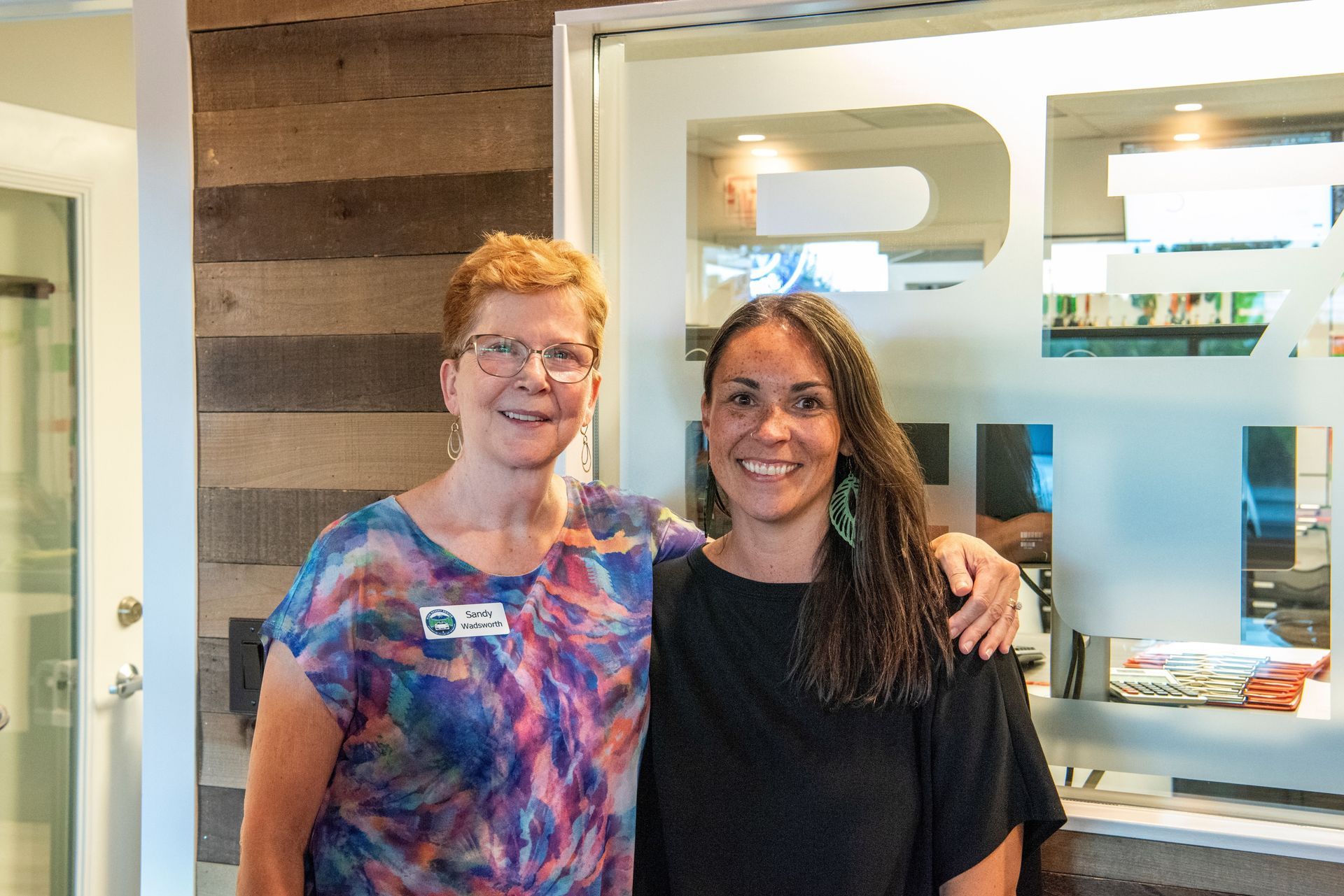 Two women smiling, standing by a glass door with 