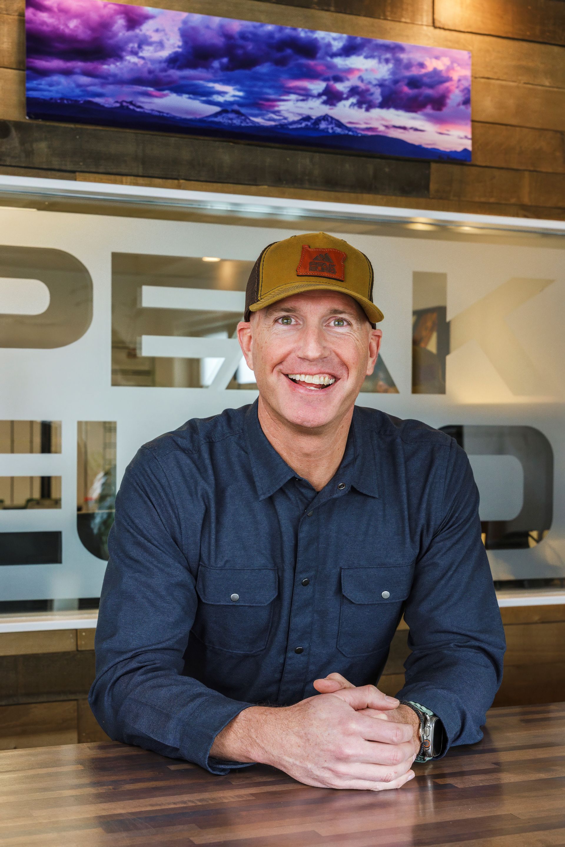 Man in a hat smiling, leaning on a counter with 