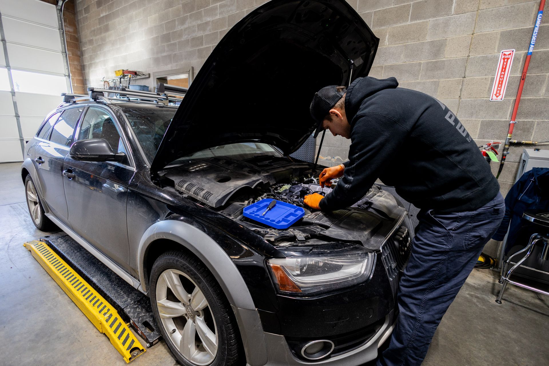 Mechanic working on a black car with the hood up in a garage.| Peak Euro