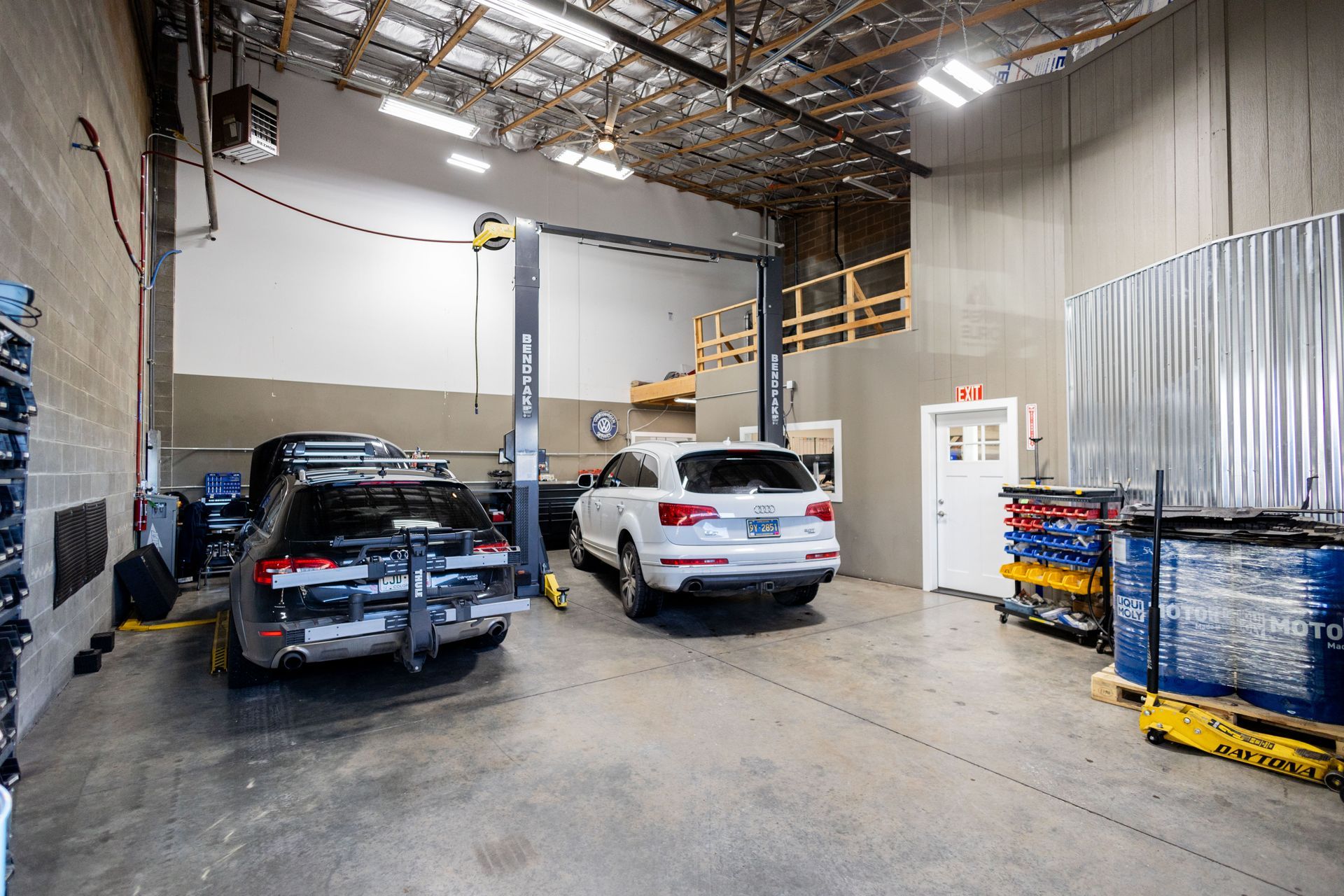 Auto repair shop: Two cars on lifts, tools, storage, and a white door.| Peak Euro