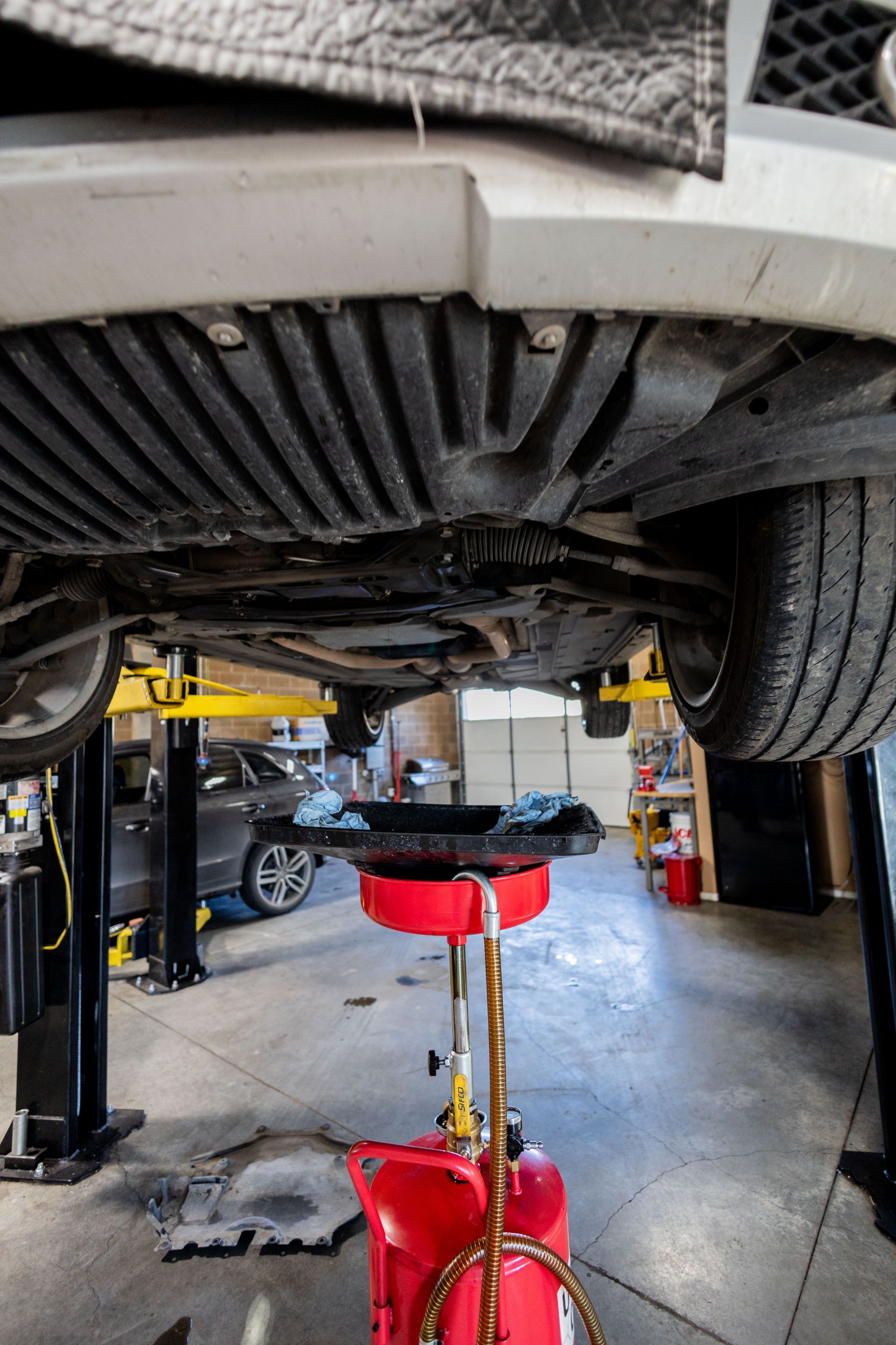 Car on a lift, oil draining into a red container in a garage.| Peak Euro