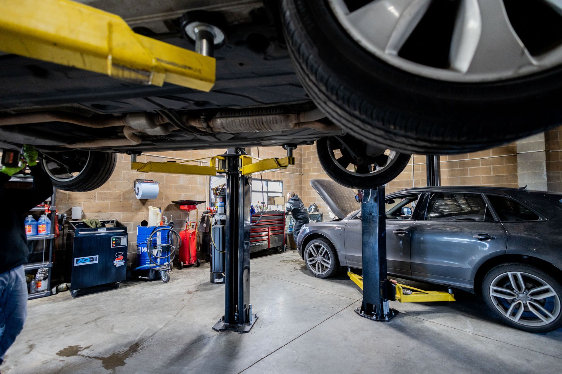 Car on a hydraulic lift in a repair shop; a mechanic works underneath.