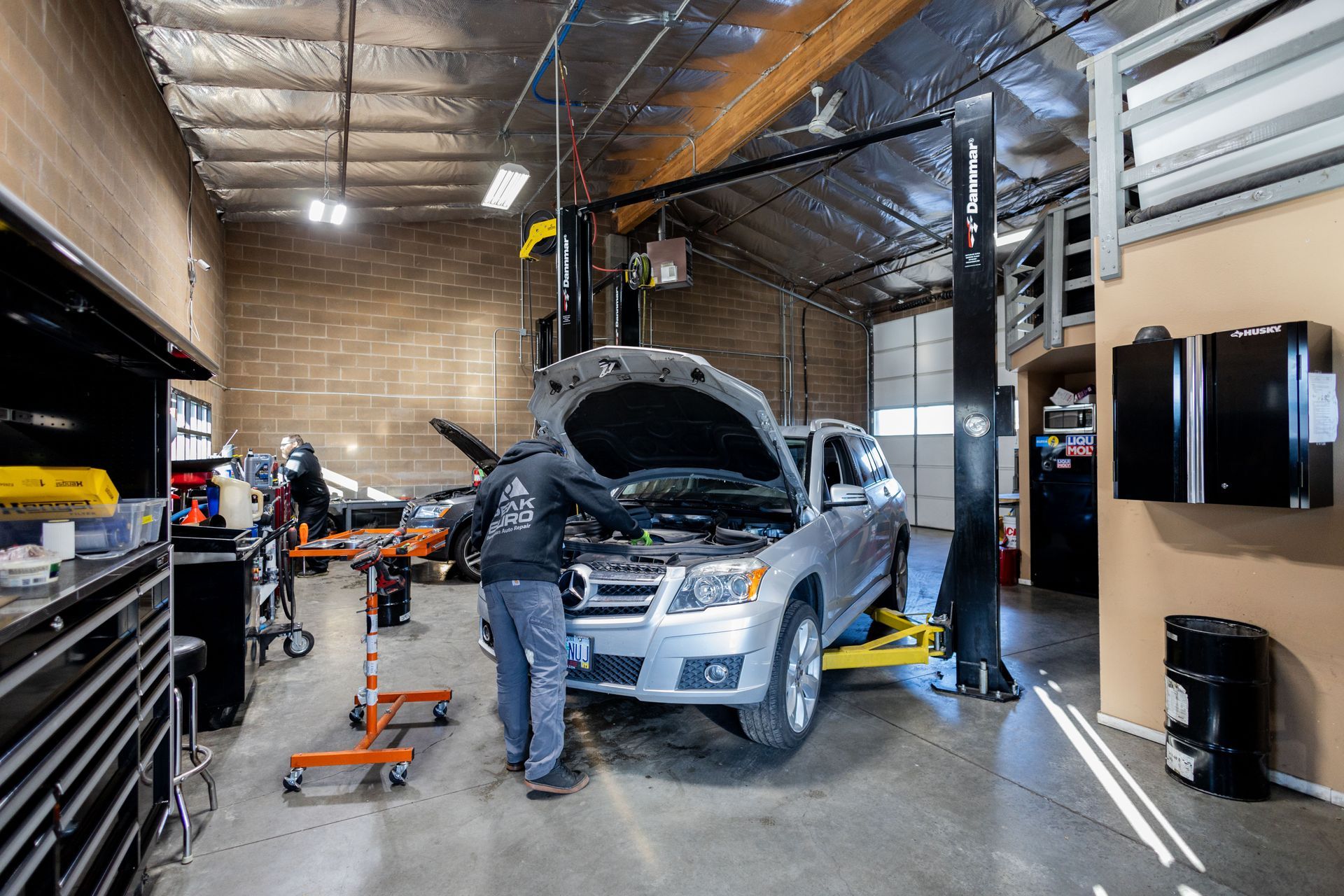 Mechanic working on a silver car in a well-lit garage; car on a lift.