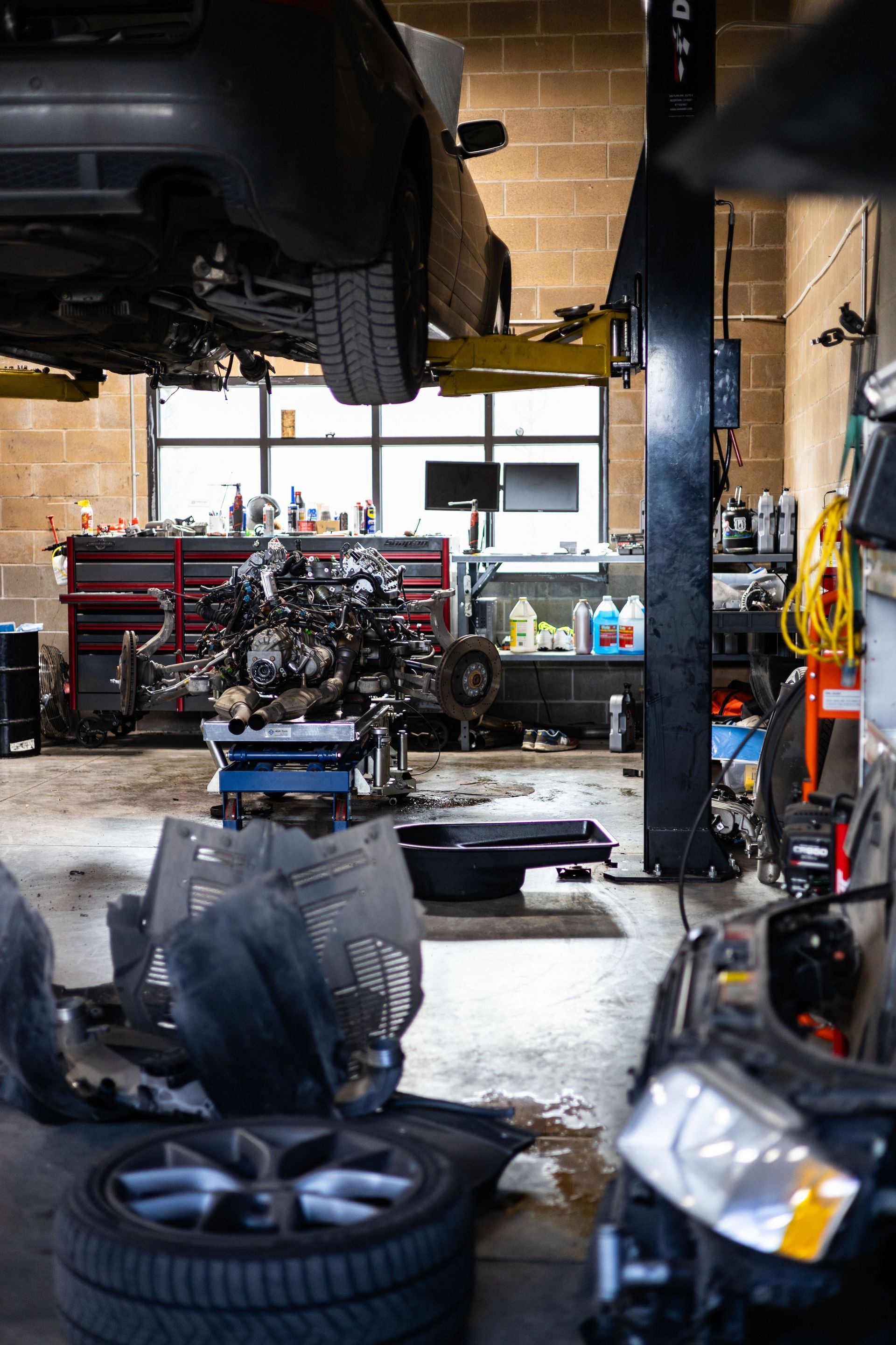 A car in a mechanic's shop is raised on a lift. Tools and parts are scattered around the shop. | Peak Euro