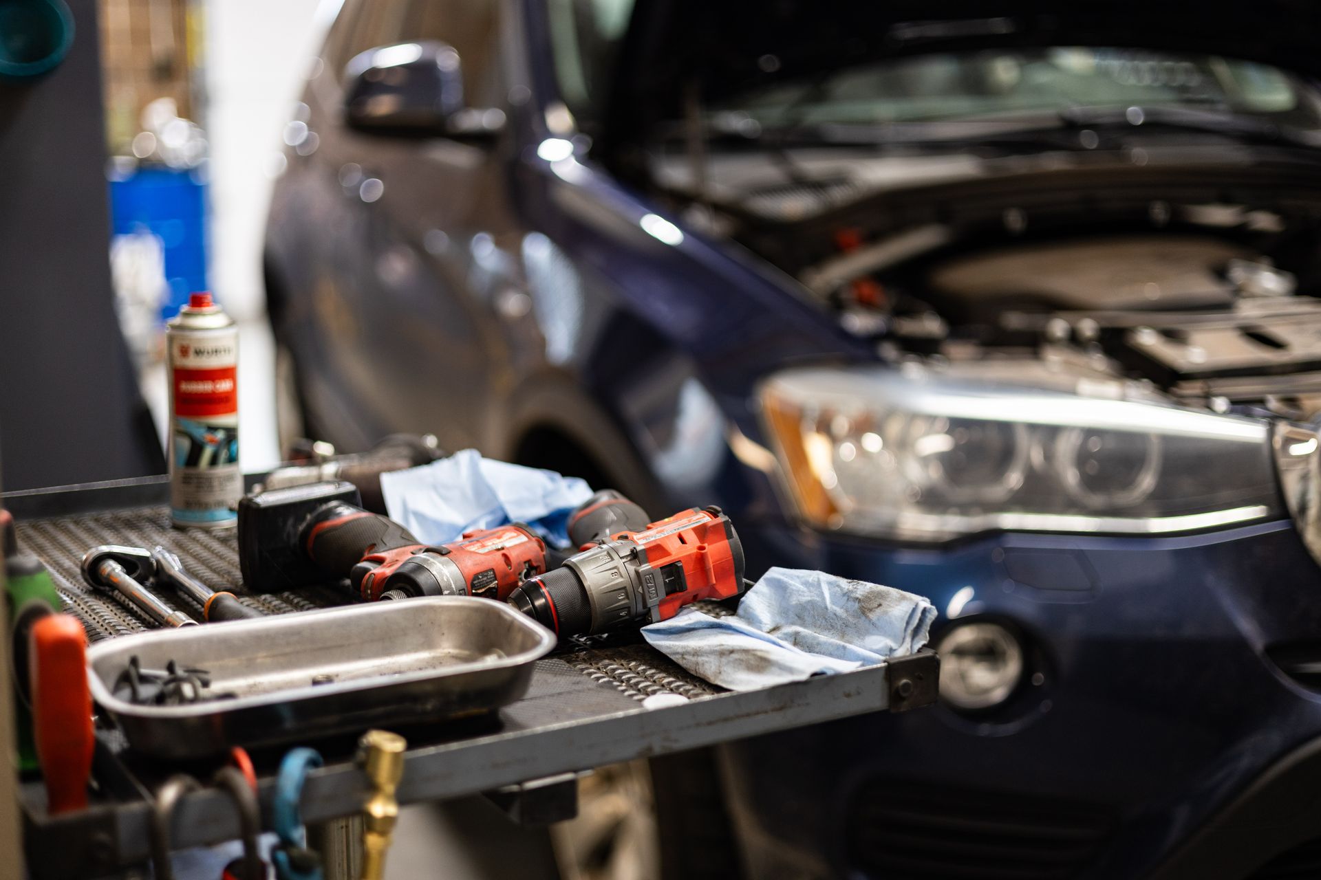 Tools on a cart near a blue car with its hood open in a garage setting. | Peak Euro