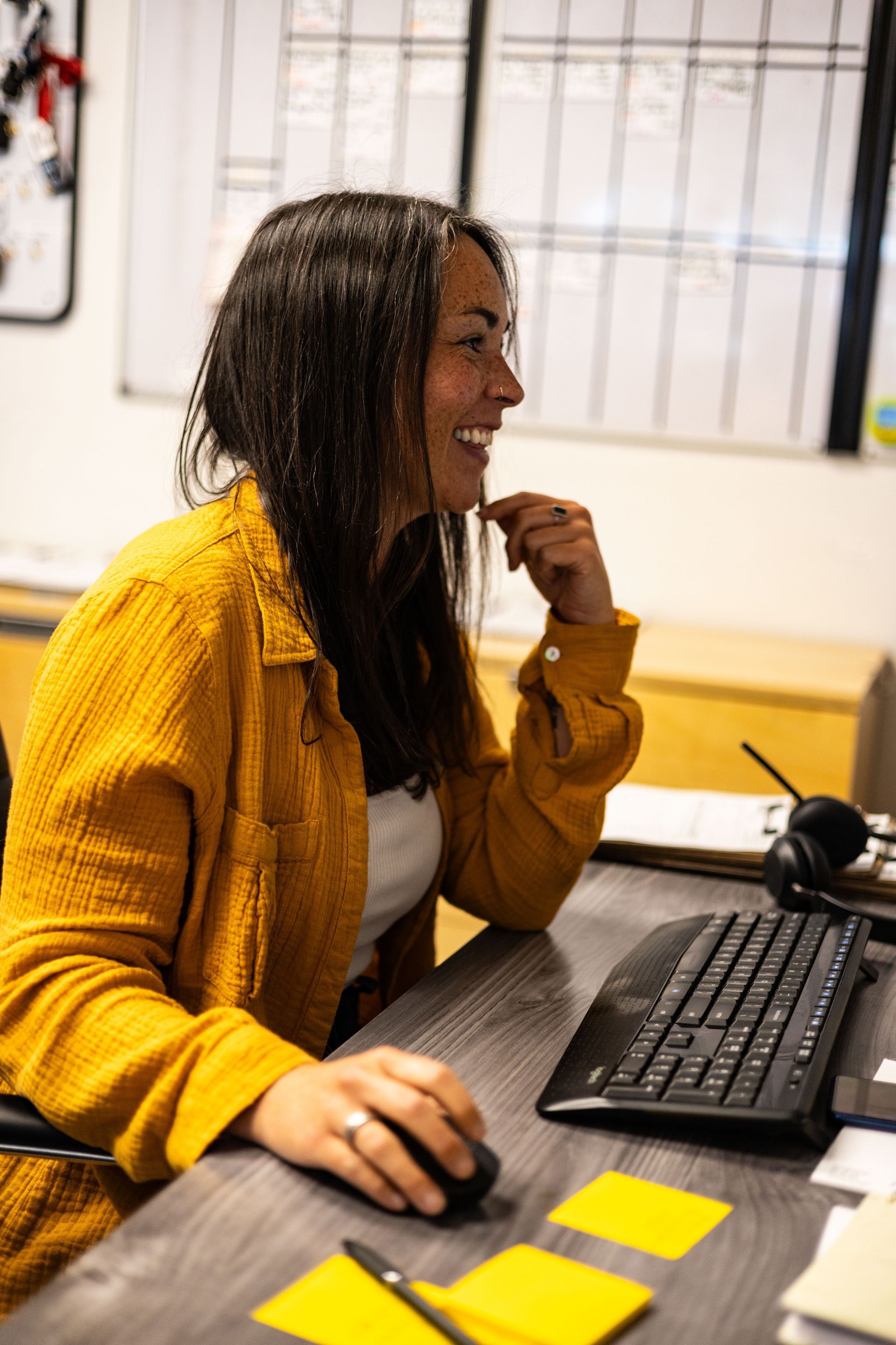 Woman smiles while working at a desk, wearing a yellow shirt. | Peak Euro