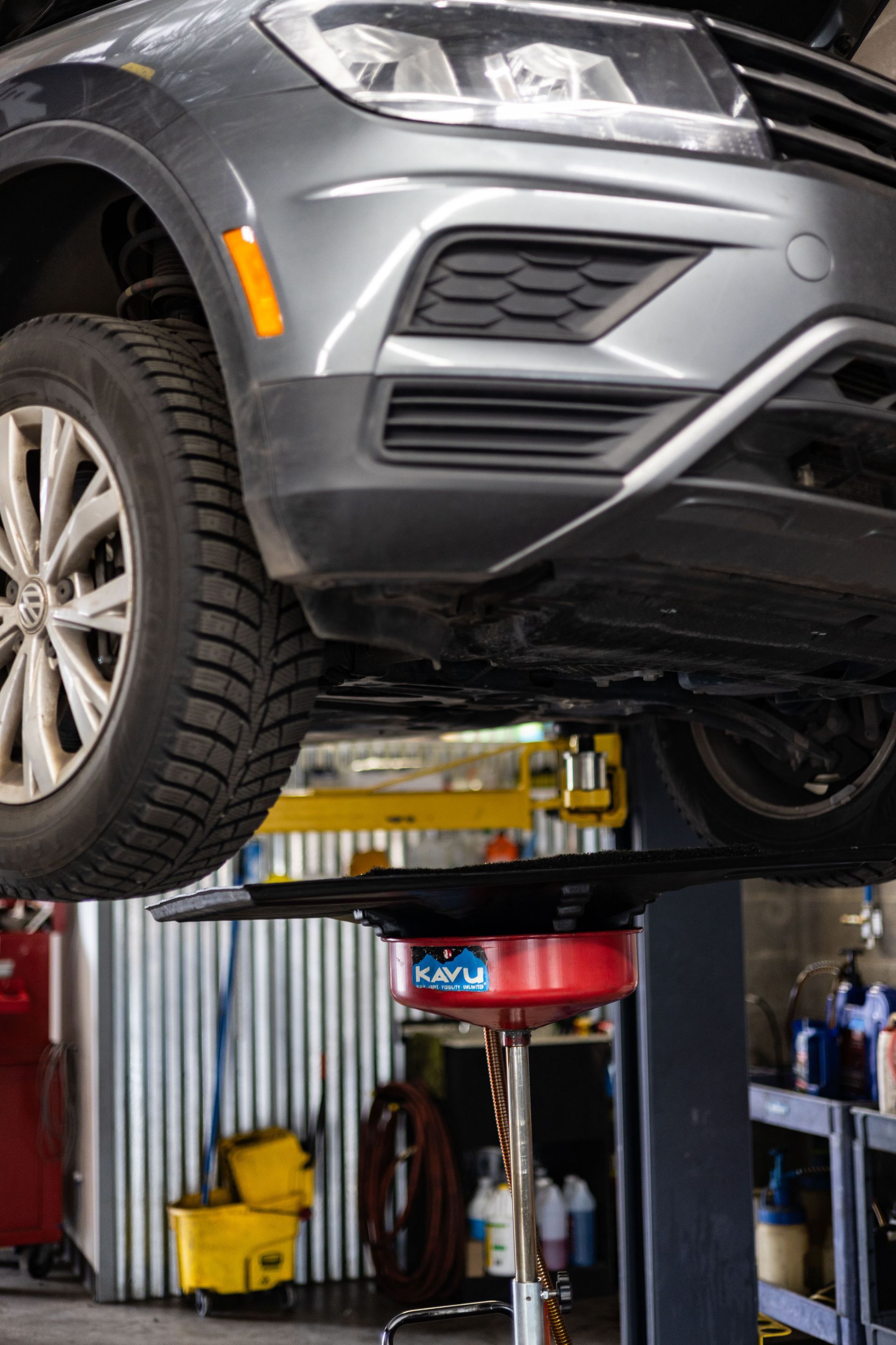 Gray SUV on a lift in a garage; oil drain pan underneath.