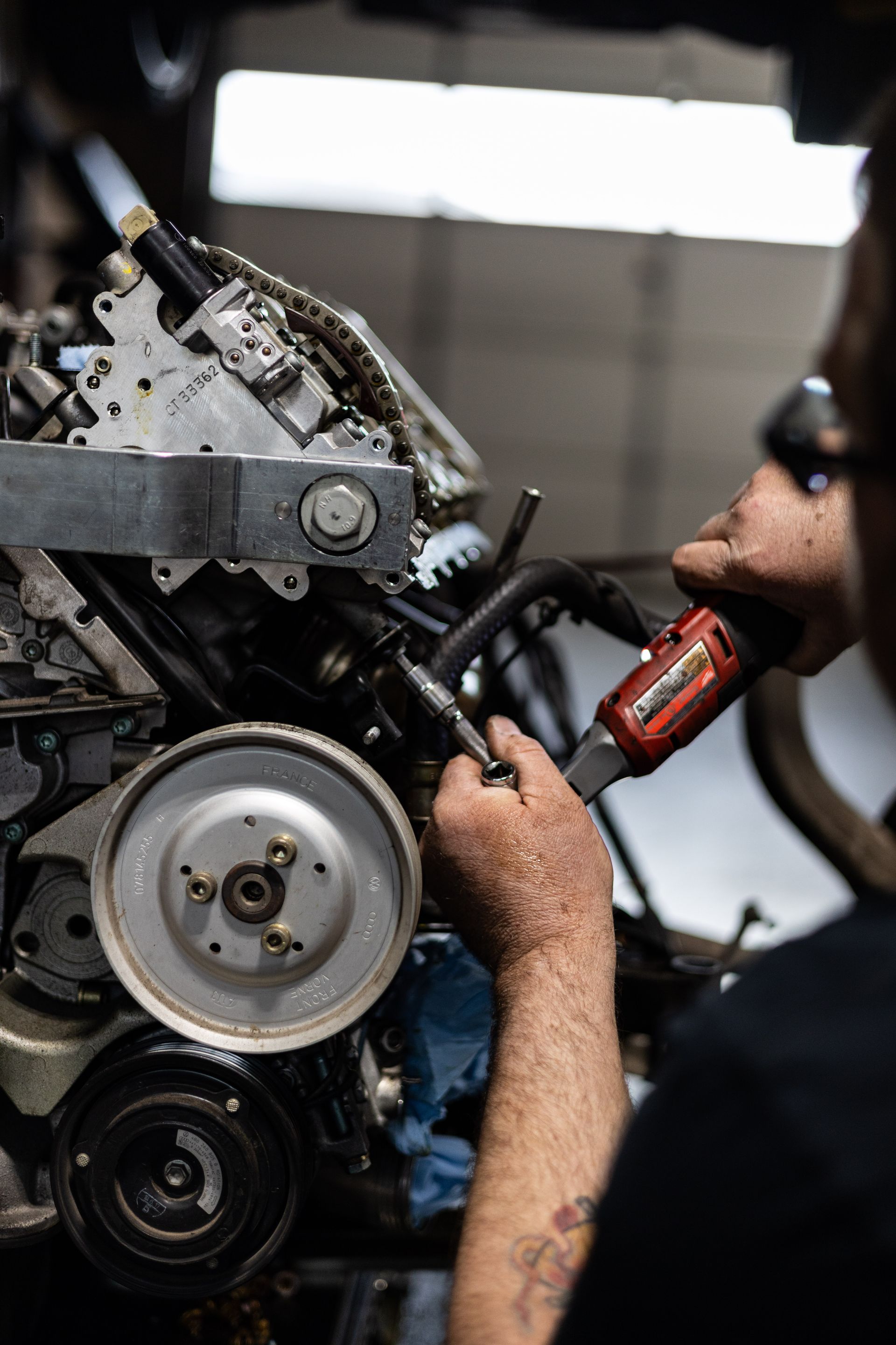 Mechanic working on an engine with a red power tool in a garage.