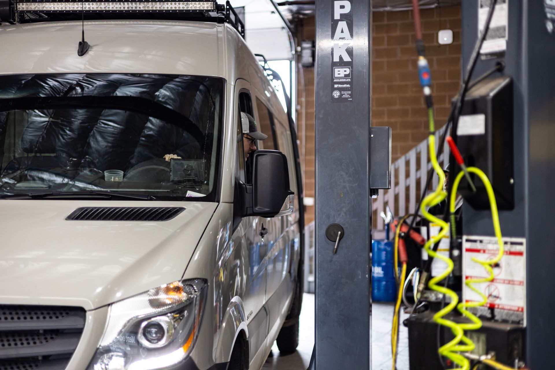 A van parked in a garage bay next to a vehicle lift. The van is light grey.