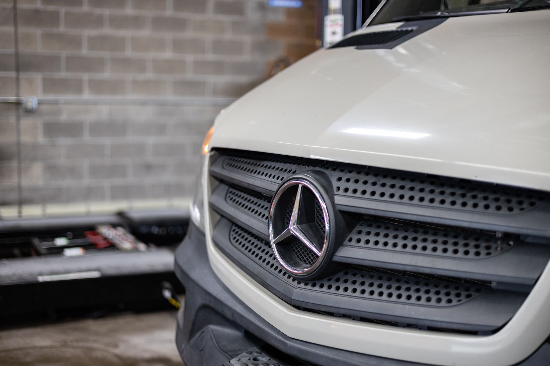 Close-up of a white Mercedes-Benz Sprinter van grill with a silver emblem, in a garage setting. | Peak Euro