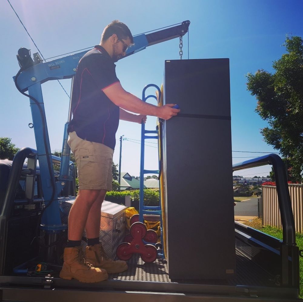 A Man Is Lifting a Refrigerator with A Crane — Toowoomba Locksmiths in Dalby, QLD
