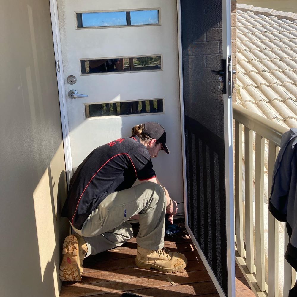 A Man Is Kneeling Down in Front of A Door — Toowoomba Locksmiths in Lockyer Valley, QLD
