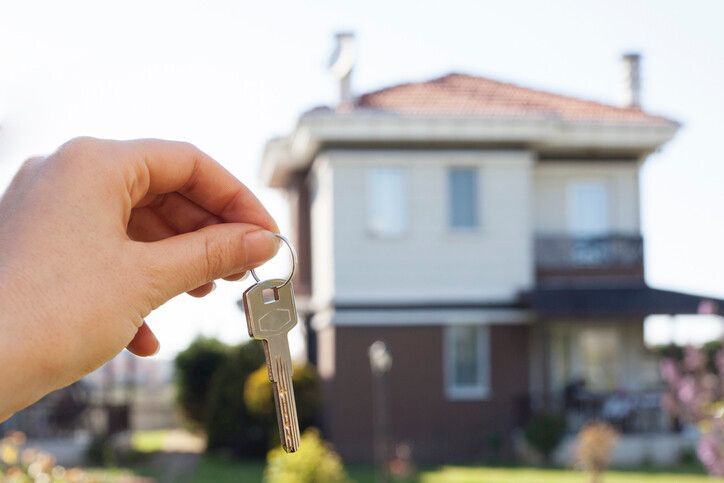 A Person Is Holding a Key in Front of A House — Toowoomba Locksmiths in Toowoomba City, QLD