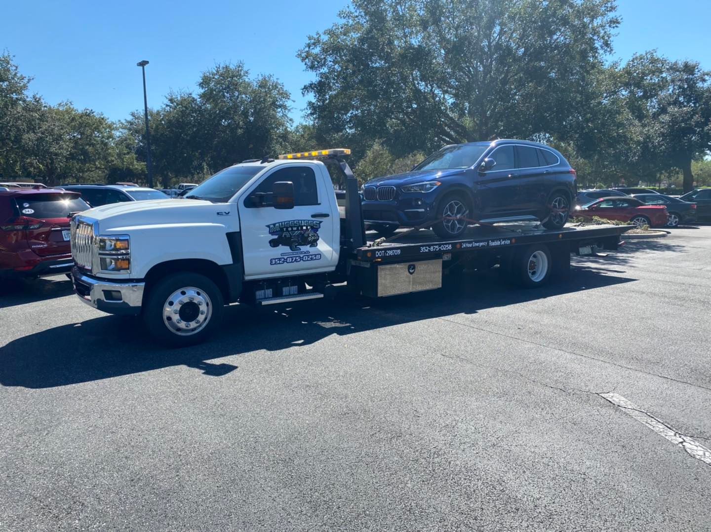 Tow truck carrying a dark blue SUV in a parking lot on a sunny day.