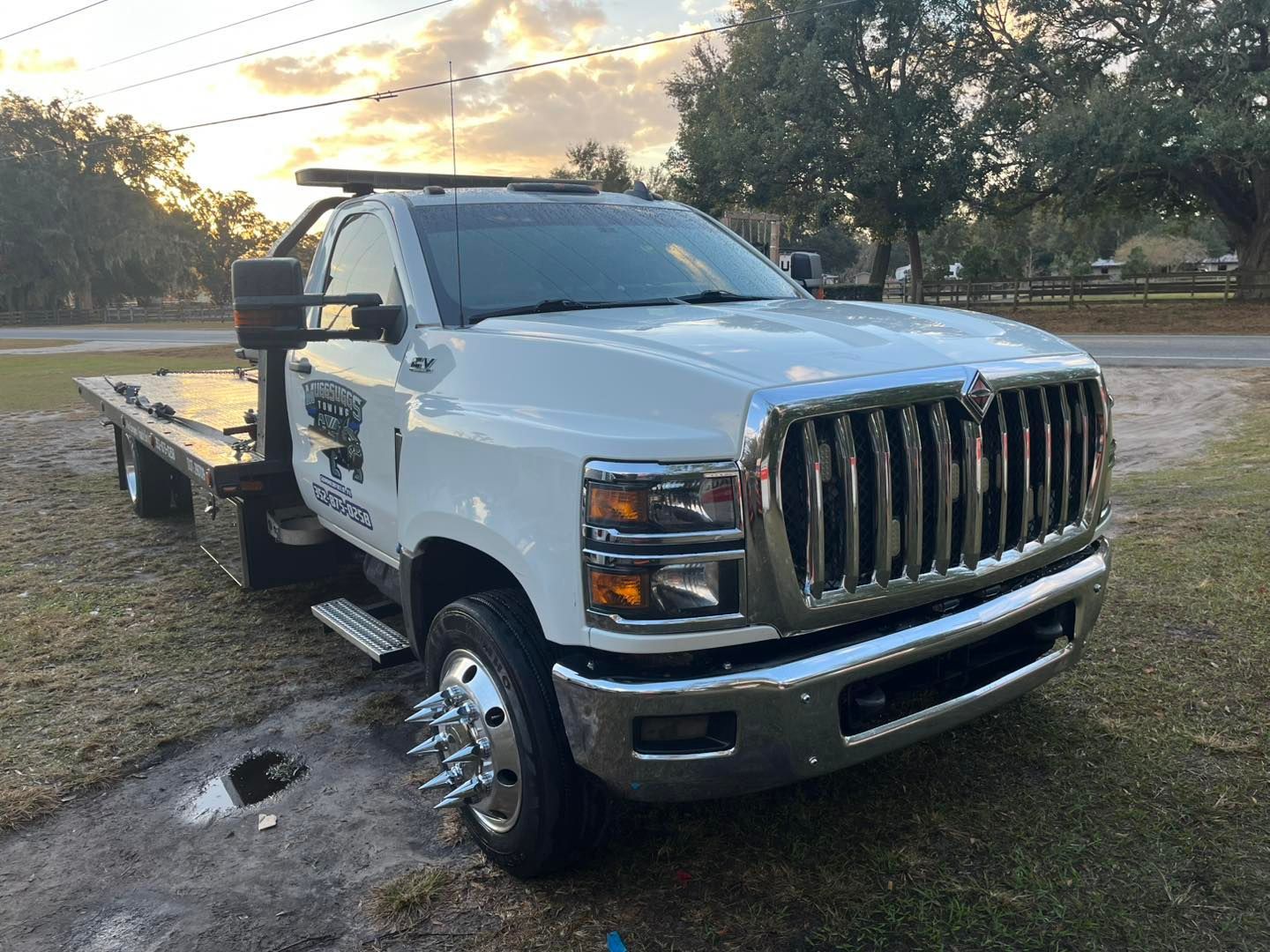 White tow truck parked on grass, near a road, under a cloudy sky.