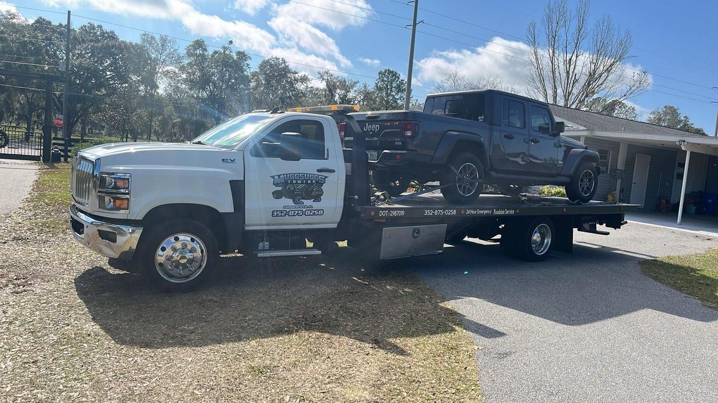 White tow truck carrying a black Jeep on a sunny day.